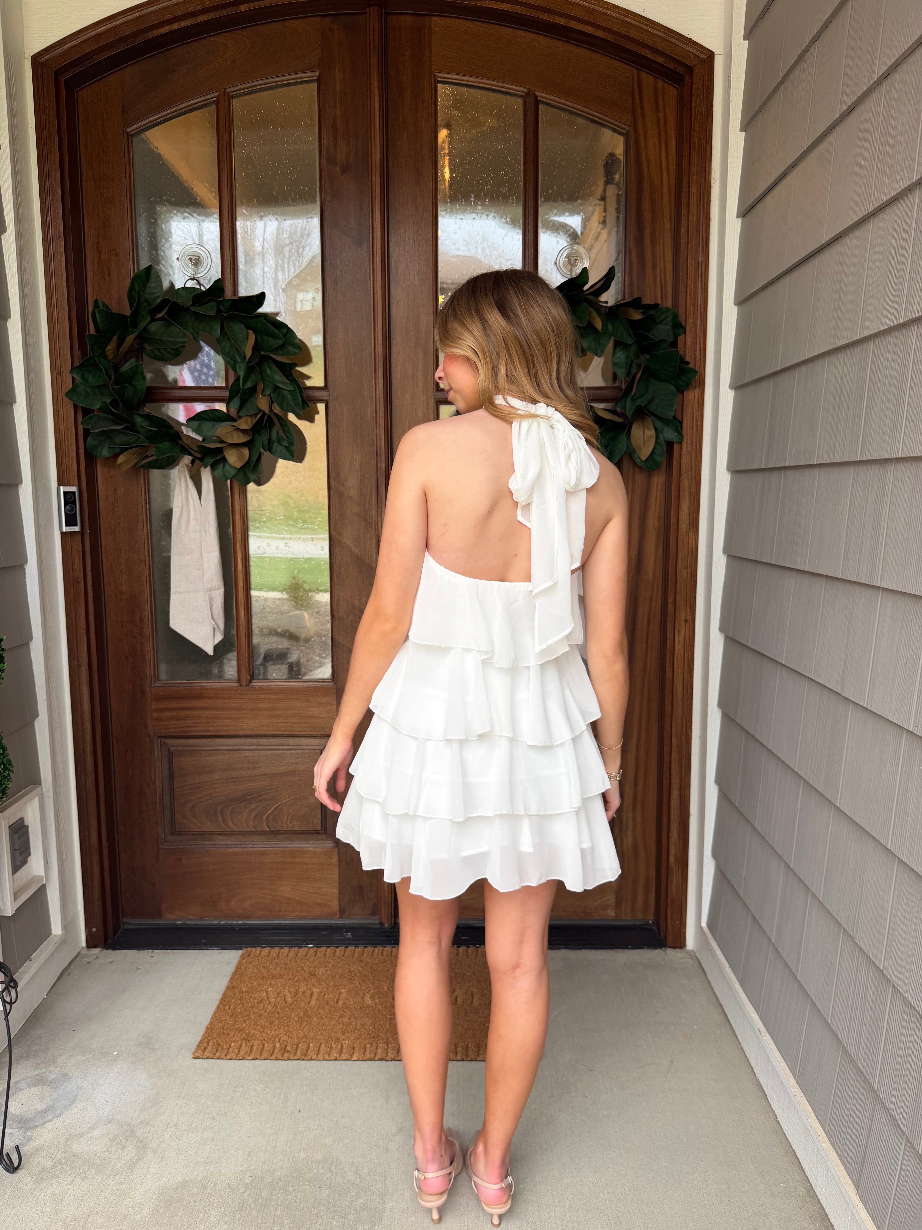 Woman in a white dress standing in front of a wooden door with wreaths.