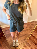 Person wearing a gray outfit with shorts and a top, standing in a room with wooden flooring.