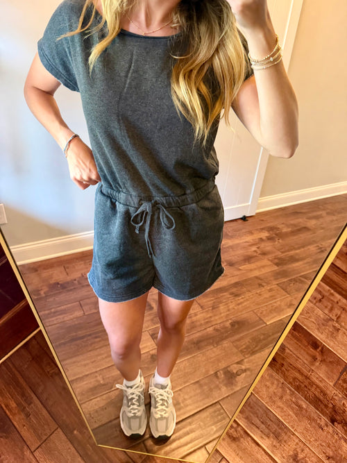 Person wearing a gray outfit with shorts and a top, standing in a room with wooden flooring.