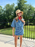 Woman wearing a denim dress and straw hat outdoors with trees in the background