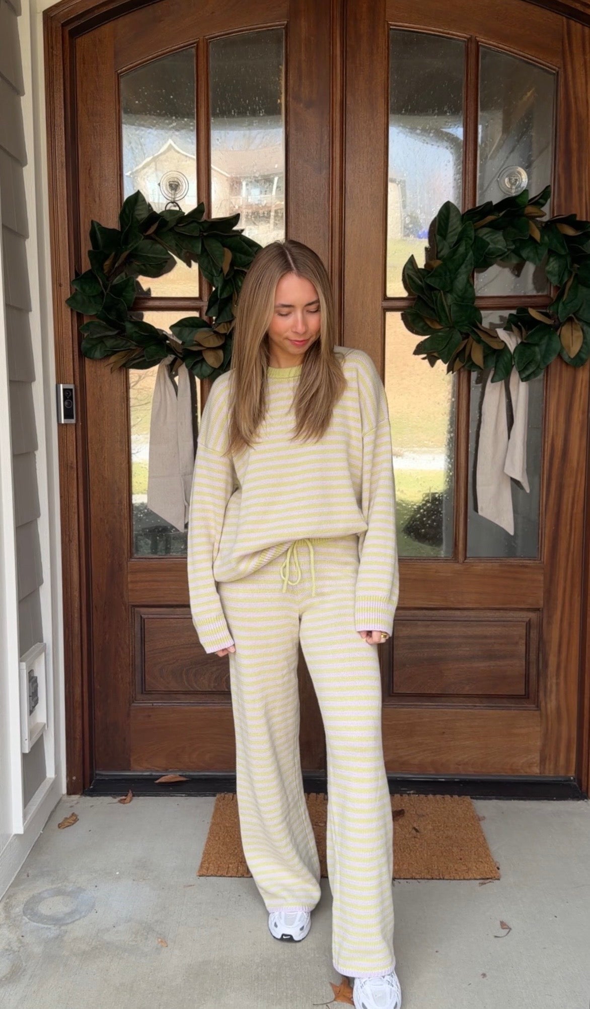 Woman in a matching striped sweater and pants standing in front of a door with wreaths.