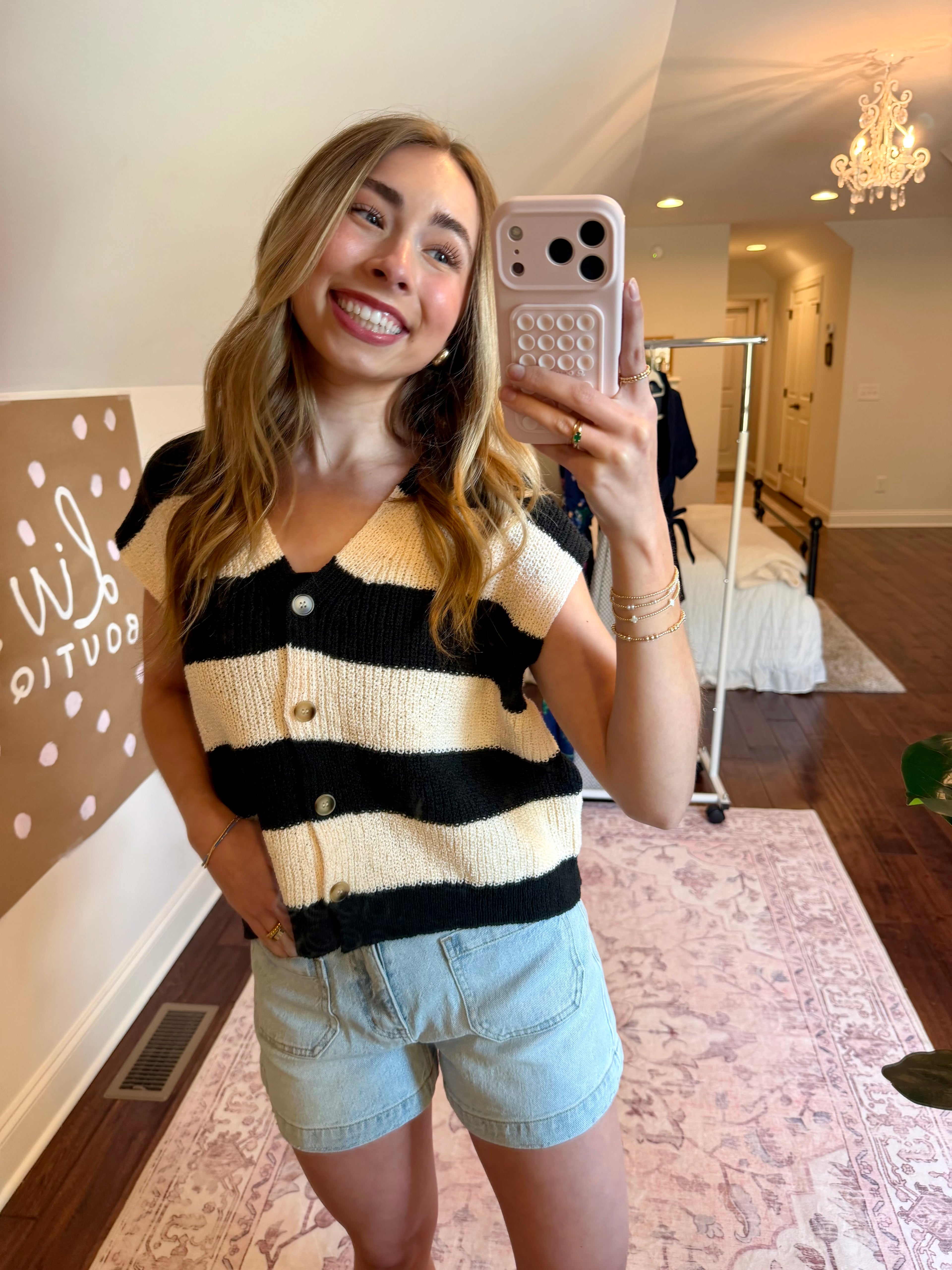 Woman taking a mirror selfie wearing a striped sweater and denim shorts in a home setting.