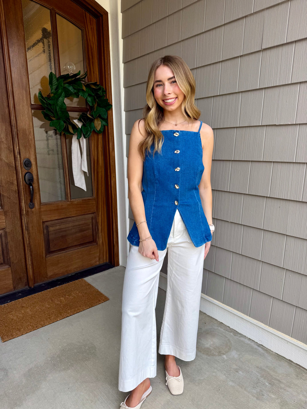 Woman wearing a blue top and white pants standing outside a house.