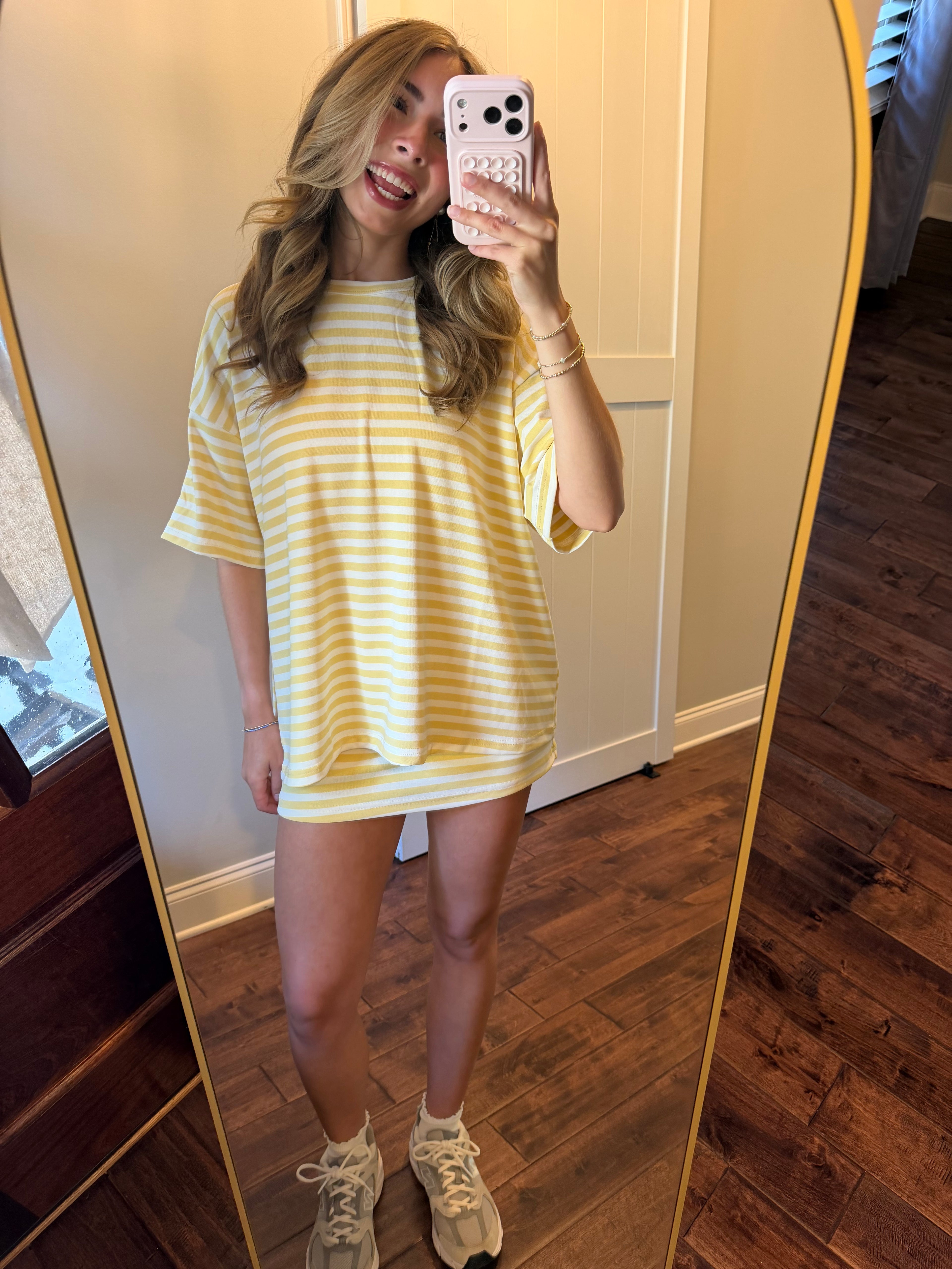 Woman taking a mirror selfie wearing a yellow and white striped dress.