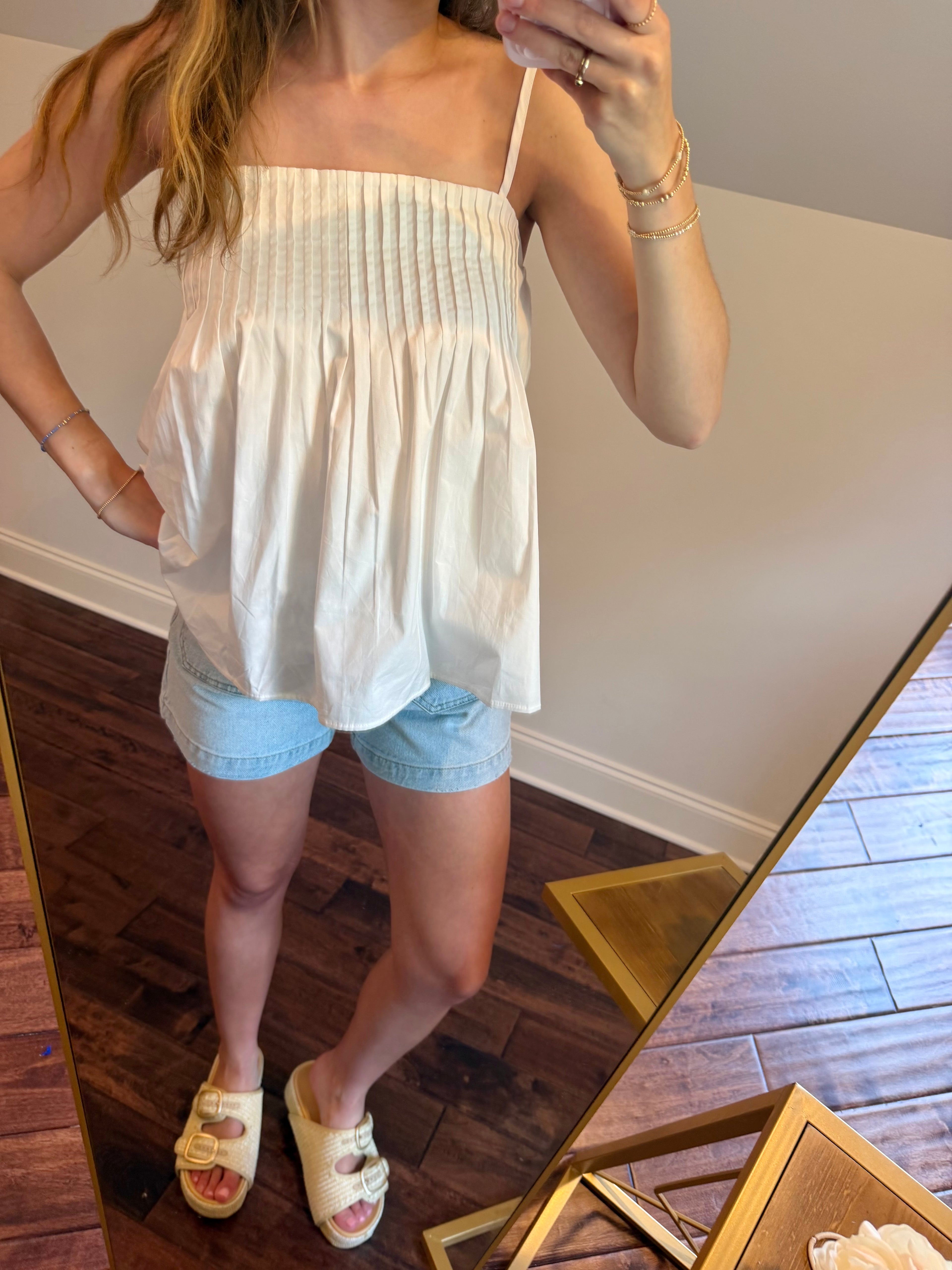 Woman wearing a white top and light blue shorts standing in front of a mirror.