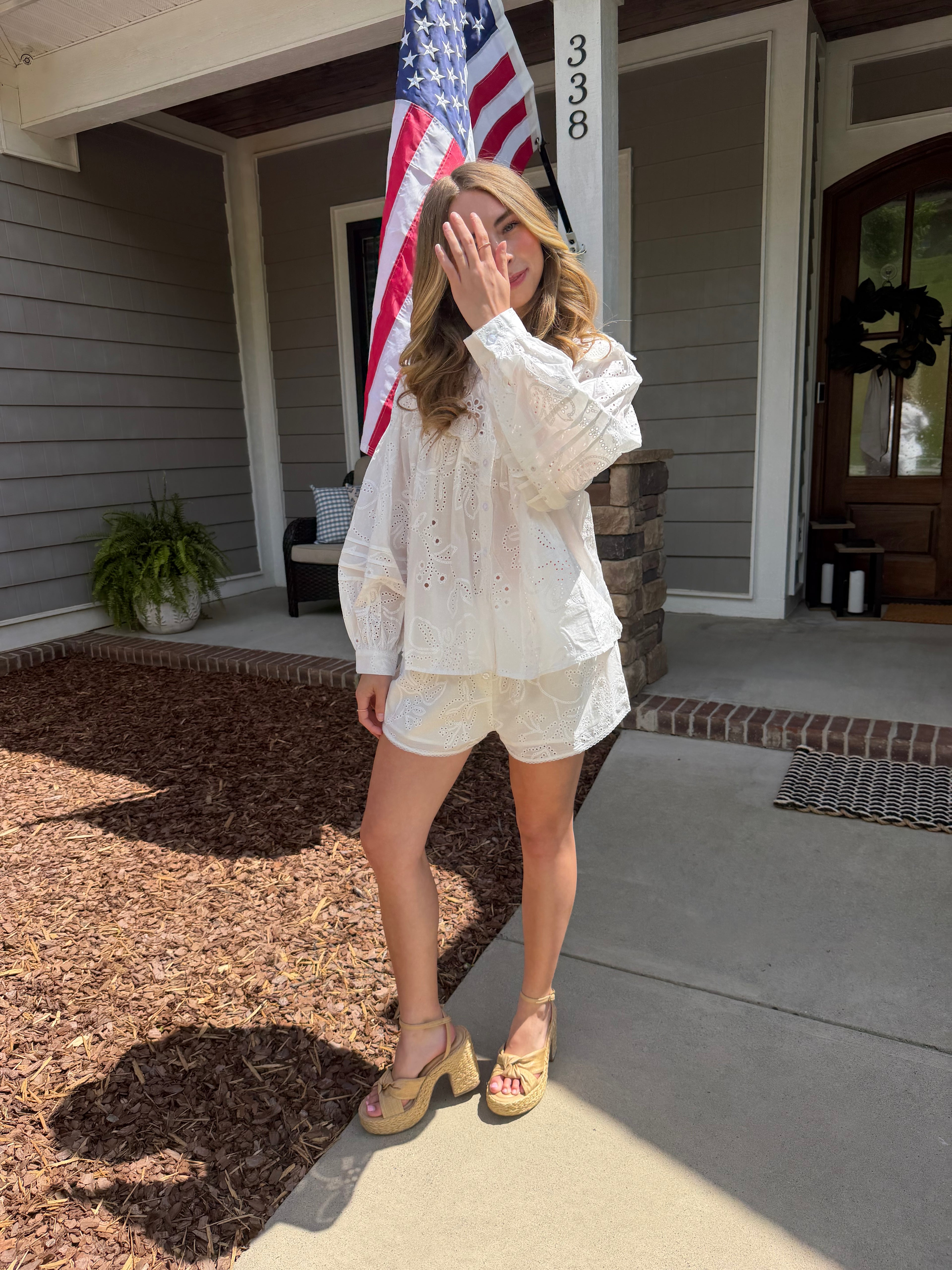 Woman in a white outfit standing on a porch with an American flag in the background