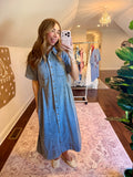 Woman taking a mirror selfie wearing a blue dress in a room with a chandelier and clothing rack.