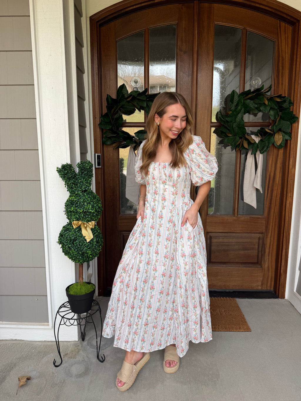Woman in a white floral dress standing in front of a wooden door with wreaths.