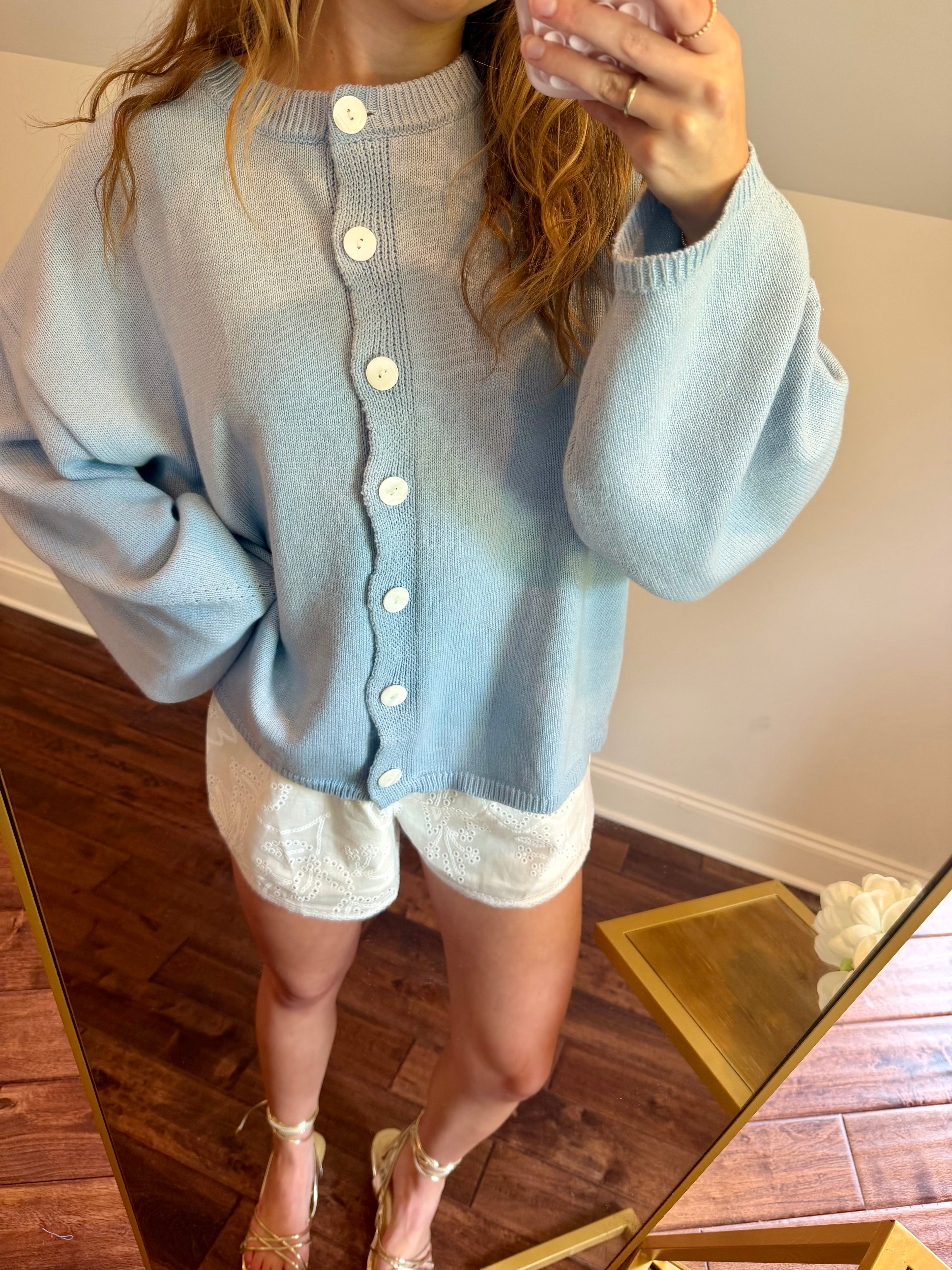 Person wearing a light blue cardigan over a white outfit, standing in a room with wooden flooring.