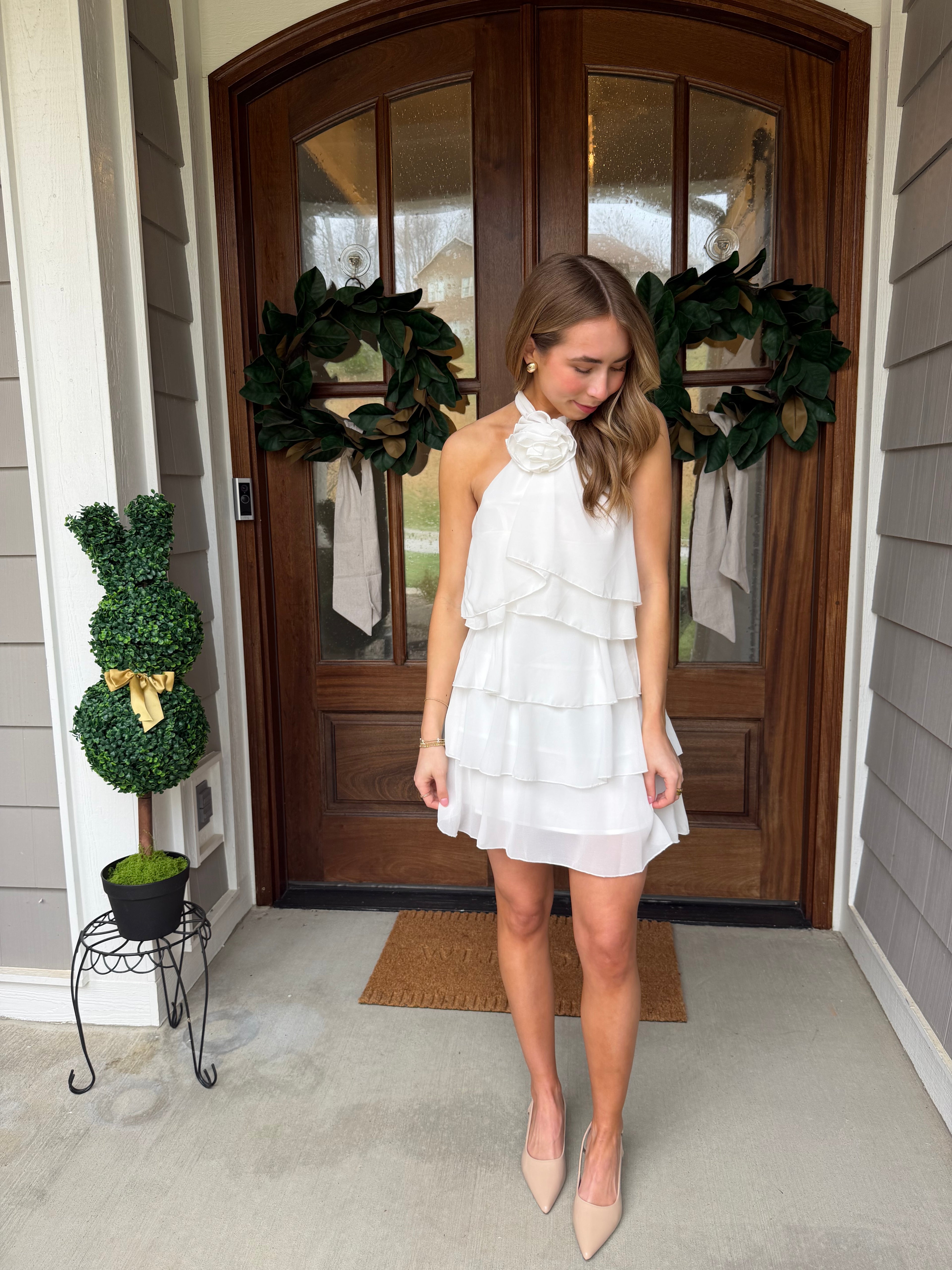 Woman in a white dress standing in front of a wooden door with wreaths.