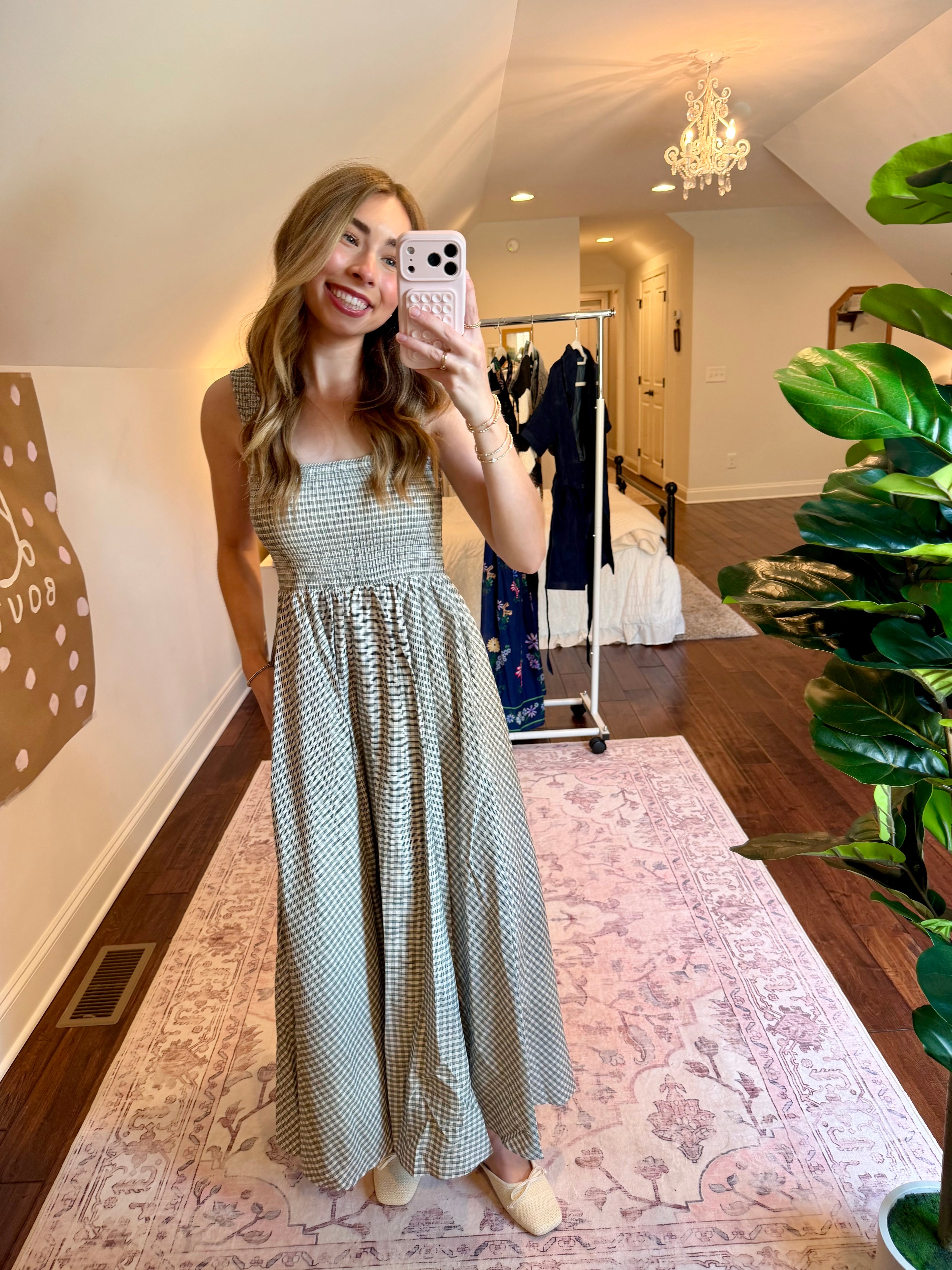 Woman taking a mirror selfie wearing a checkered dress in a home setting.