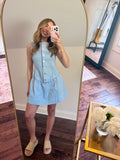 Woman taking a mirror selfie wearing a light blue dress in a room with wooden flooring.