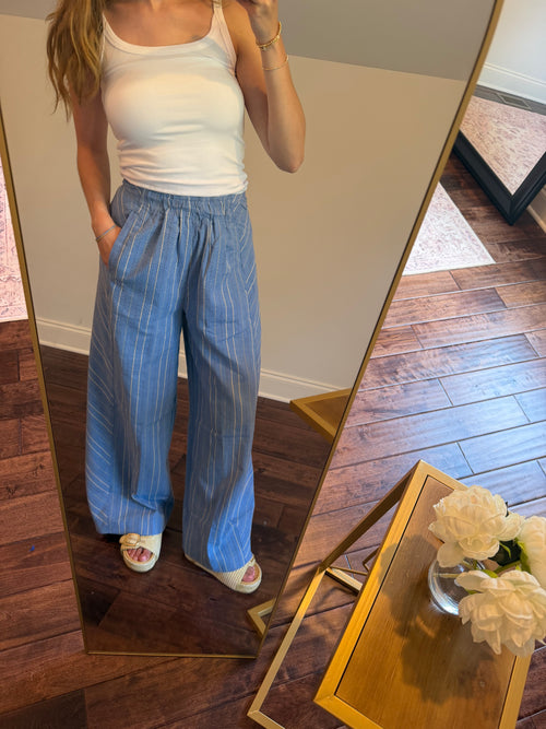 Person wearing a white tank top and blue pants standing in front of a mirror.