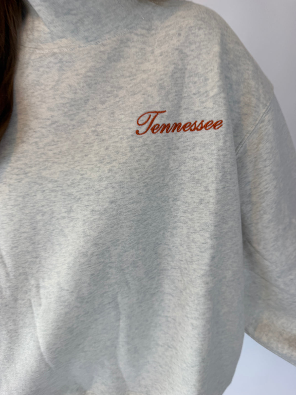 Close-up of a light heather gray sweatshirt with the word 'Tennessee' embroidered in brown cursive across the chest.