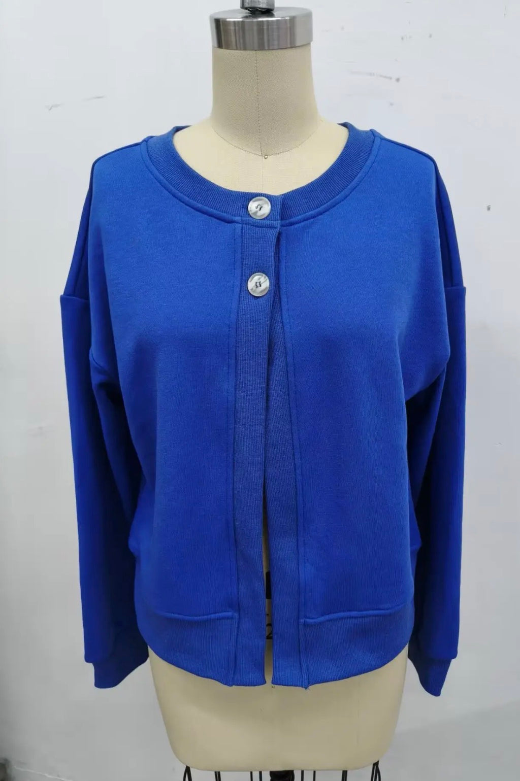 A bright royal blue long-sleeve cardigan sweater displayed on a beige dress form mannequin against a plain white wall.