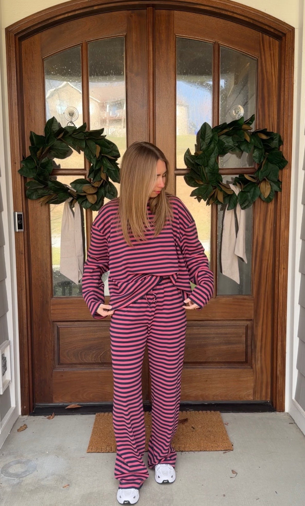 Person wearing a striped outfit standing in front of a wooden door with wreaths.