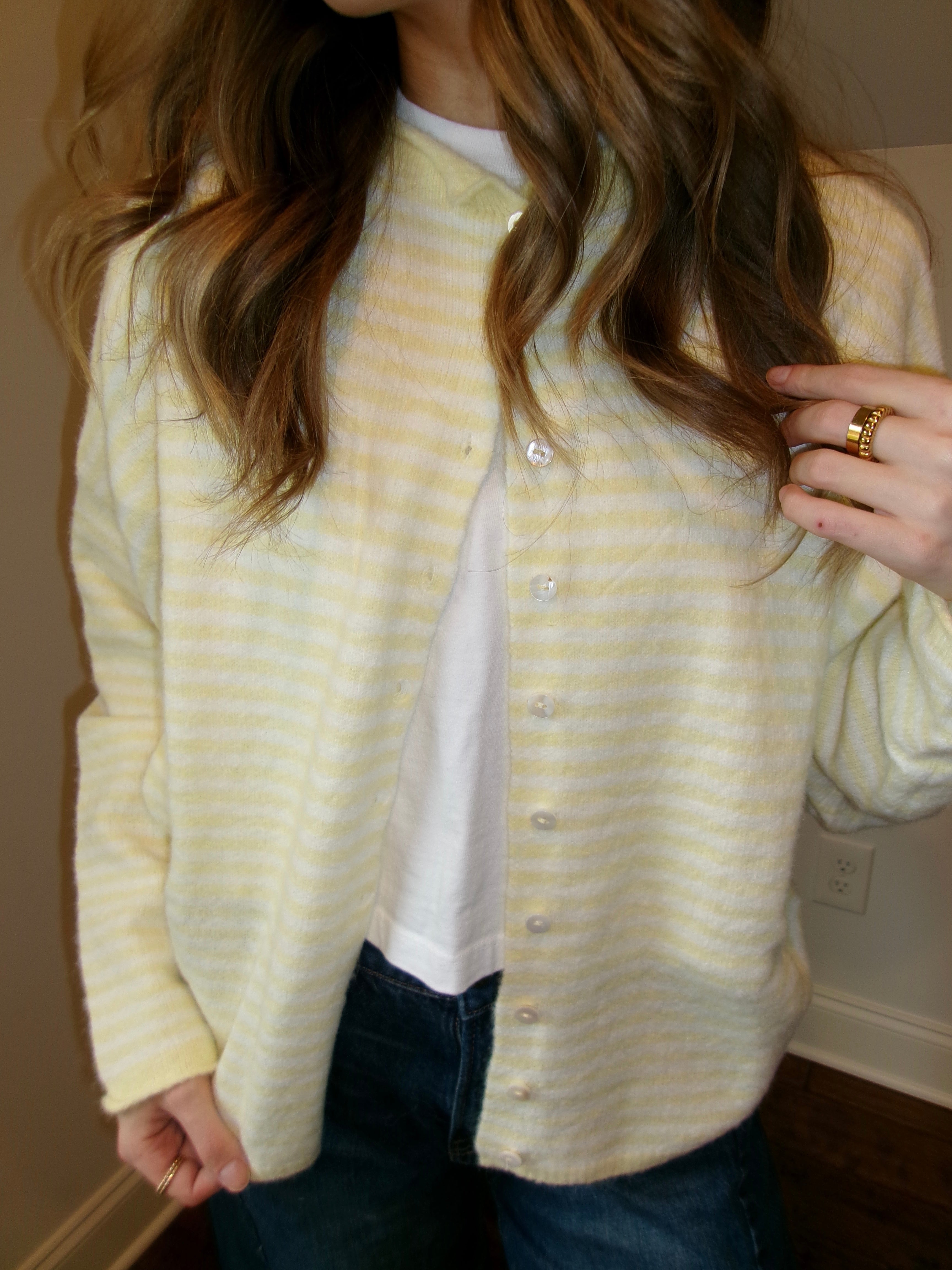 Person wearing a yellow striped cardigan over a white shirt, standing indoors.