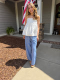 Woman standing on a porch wearing a white top and blue striped pants, with an American flag in the background.