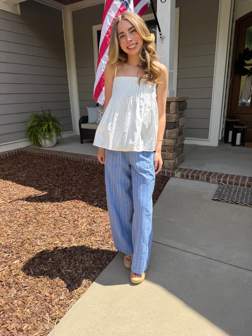Woman standing on a porch wearing a white top and blue striped pants, with an American flag in the background.