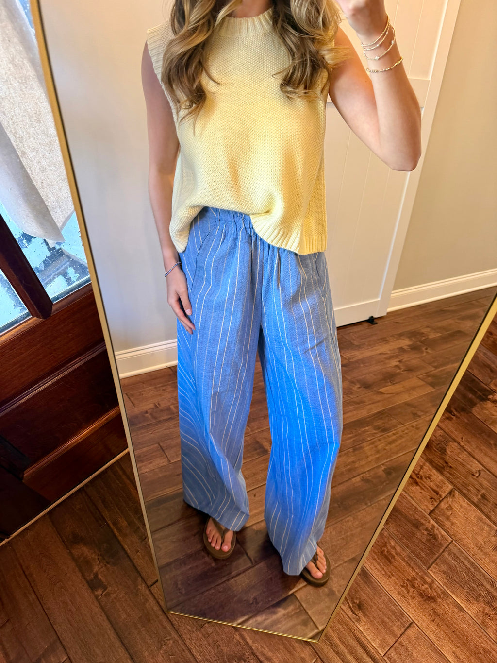 Person wearing a yellow sleeveless top and blue striped pants standing in front of a mirror.