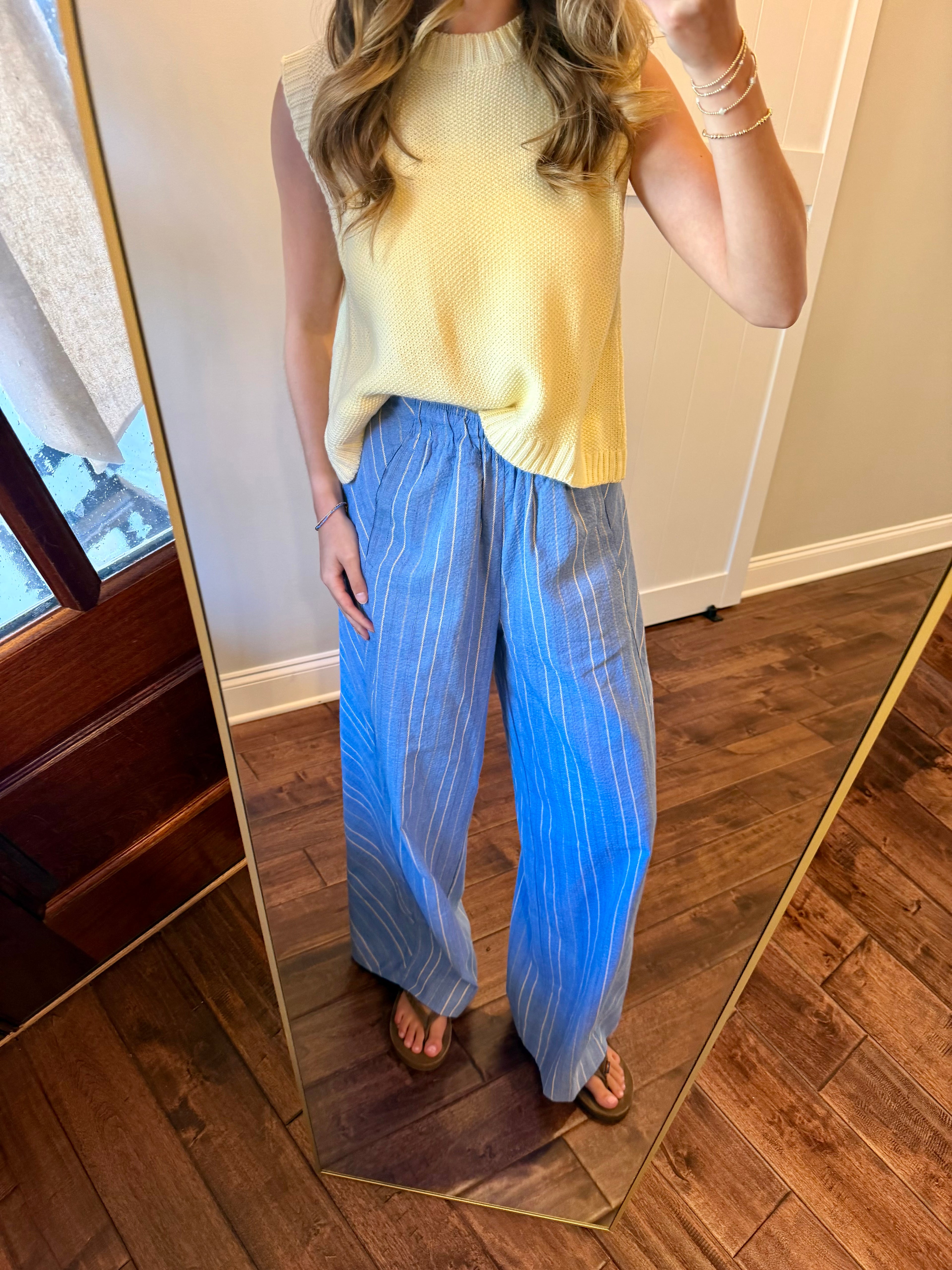 Person wearing a yellow sleeveless top and blue striped pants standing in front of a mirror.