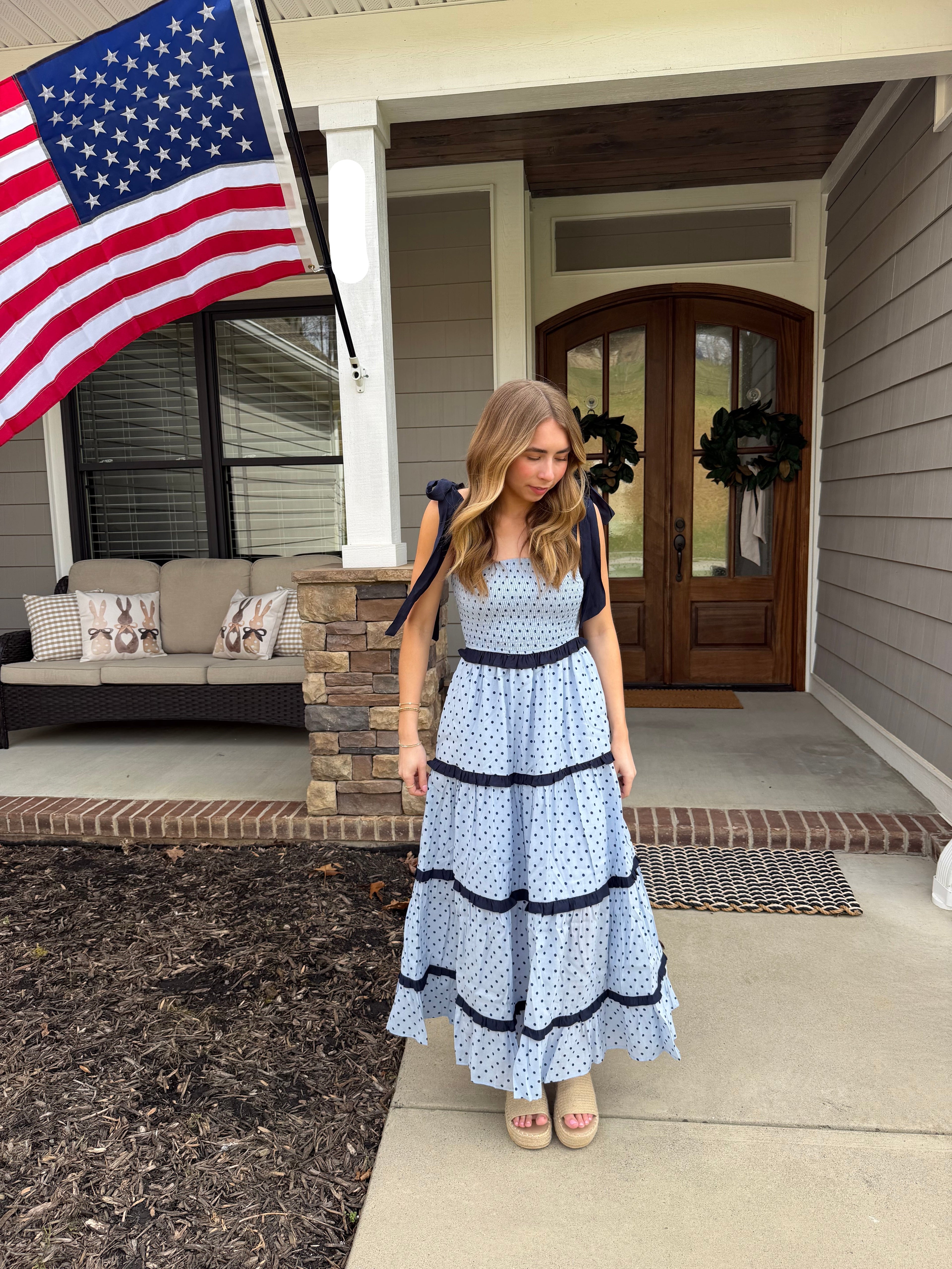 Woman in a blue and navy polka dot dress outside of a house. 