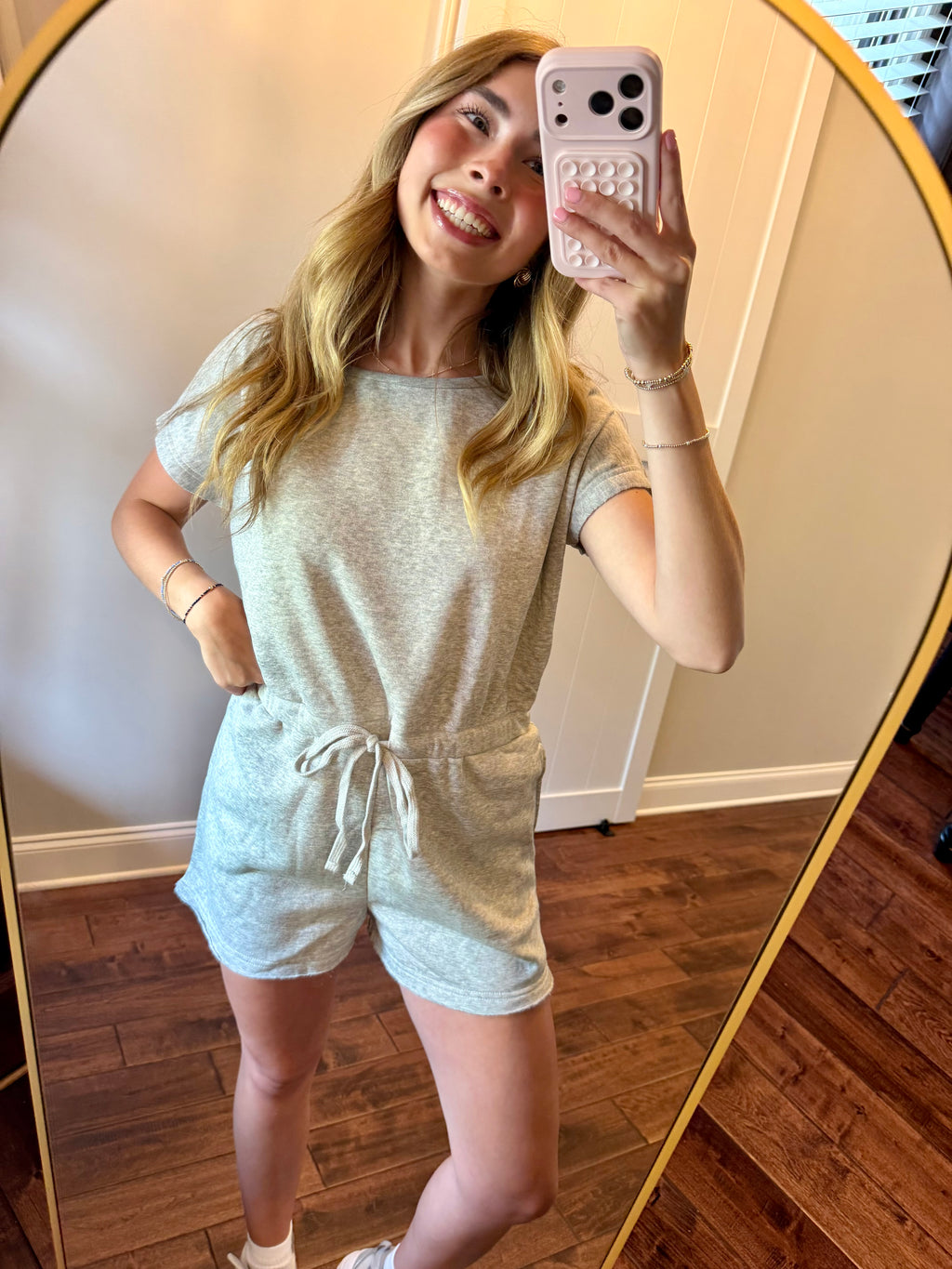 Woman taking a mirror selfie wearing a light gray romper.