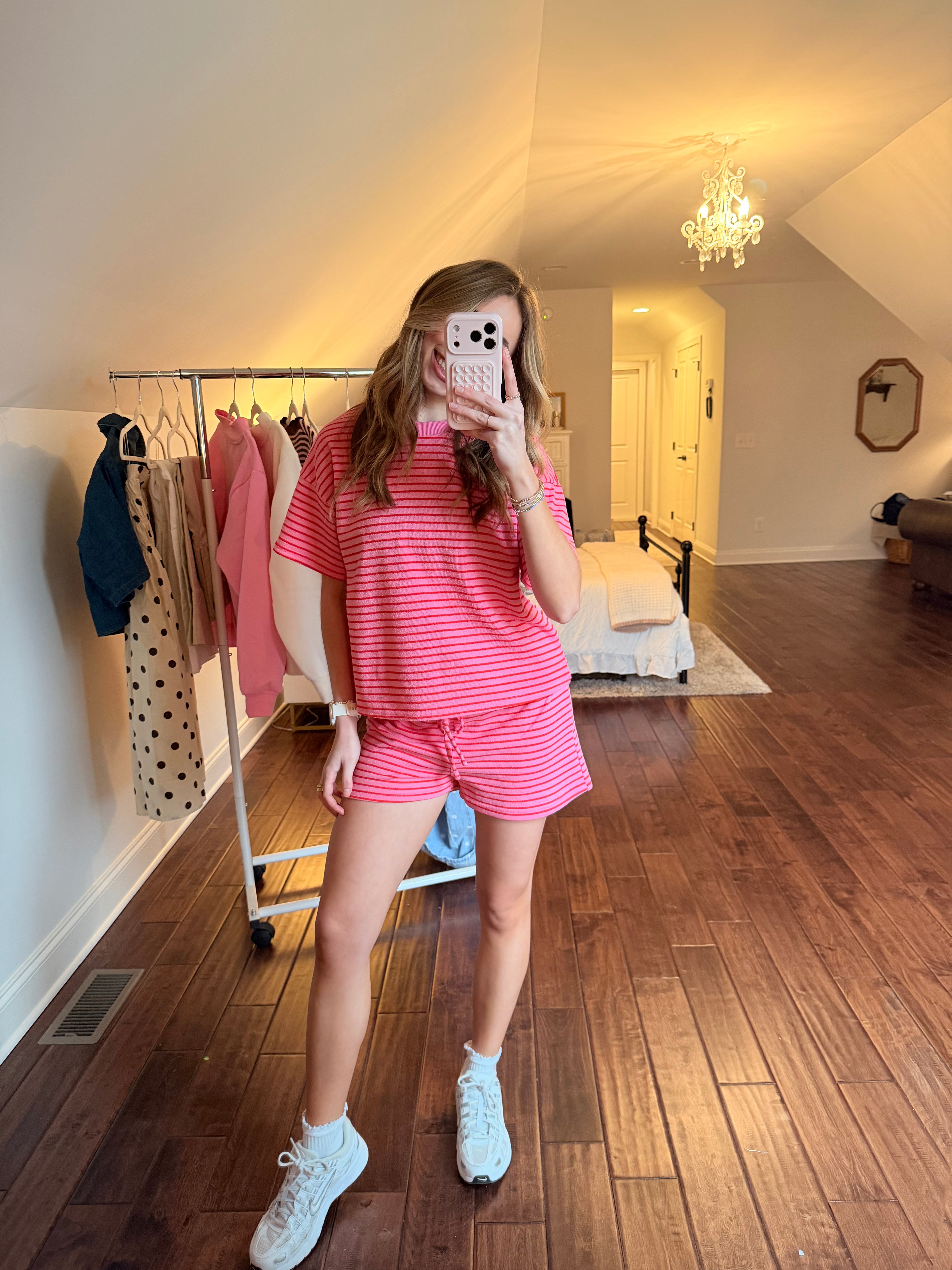 Person taking a mirror selfie wearing a pink matching set in a room with wooden floor and white walls.