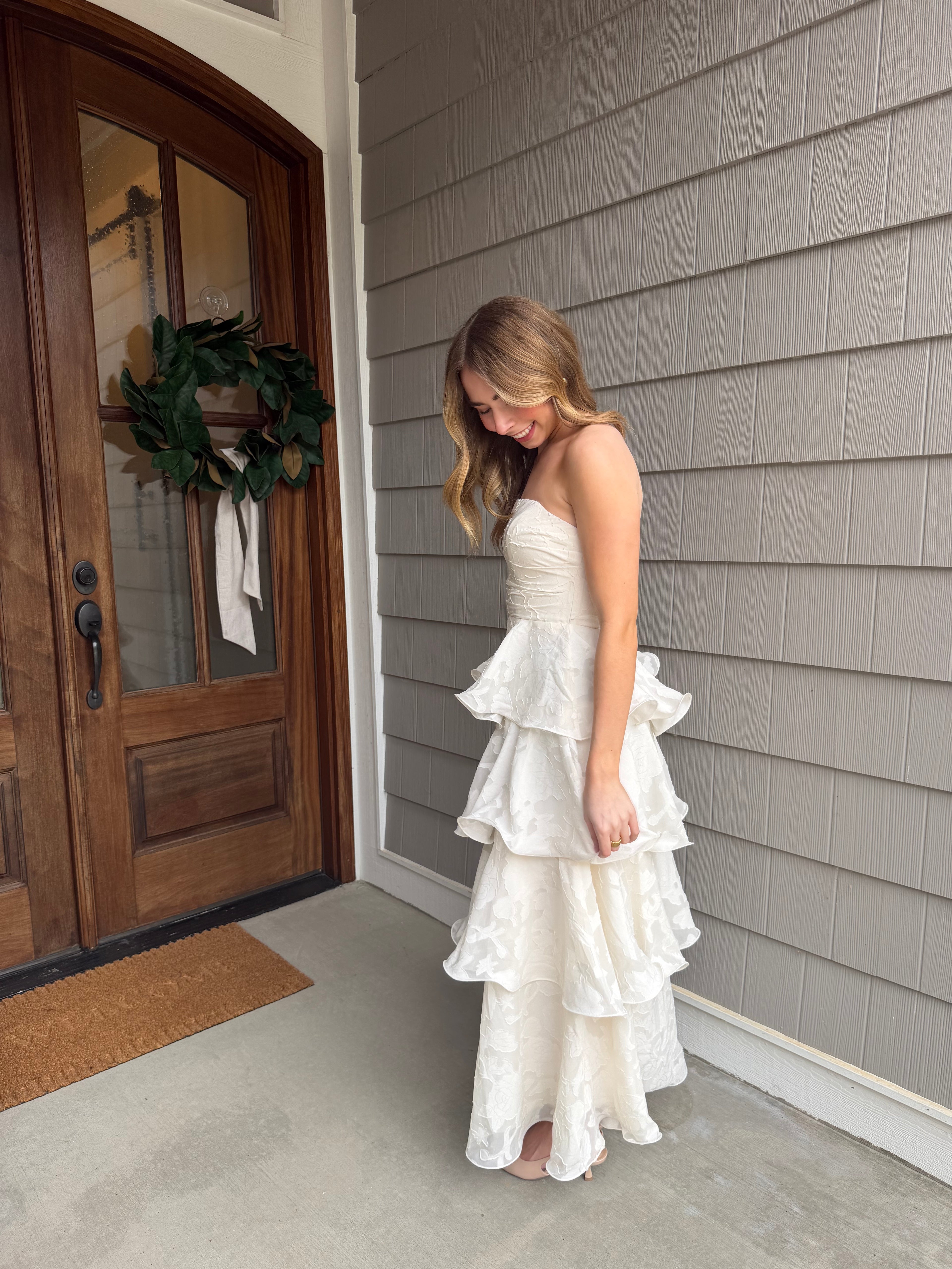 Woman in a white dress standing in front of a wooden door with a wreath.
