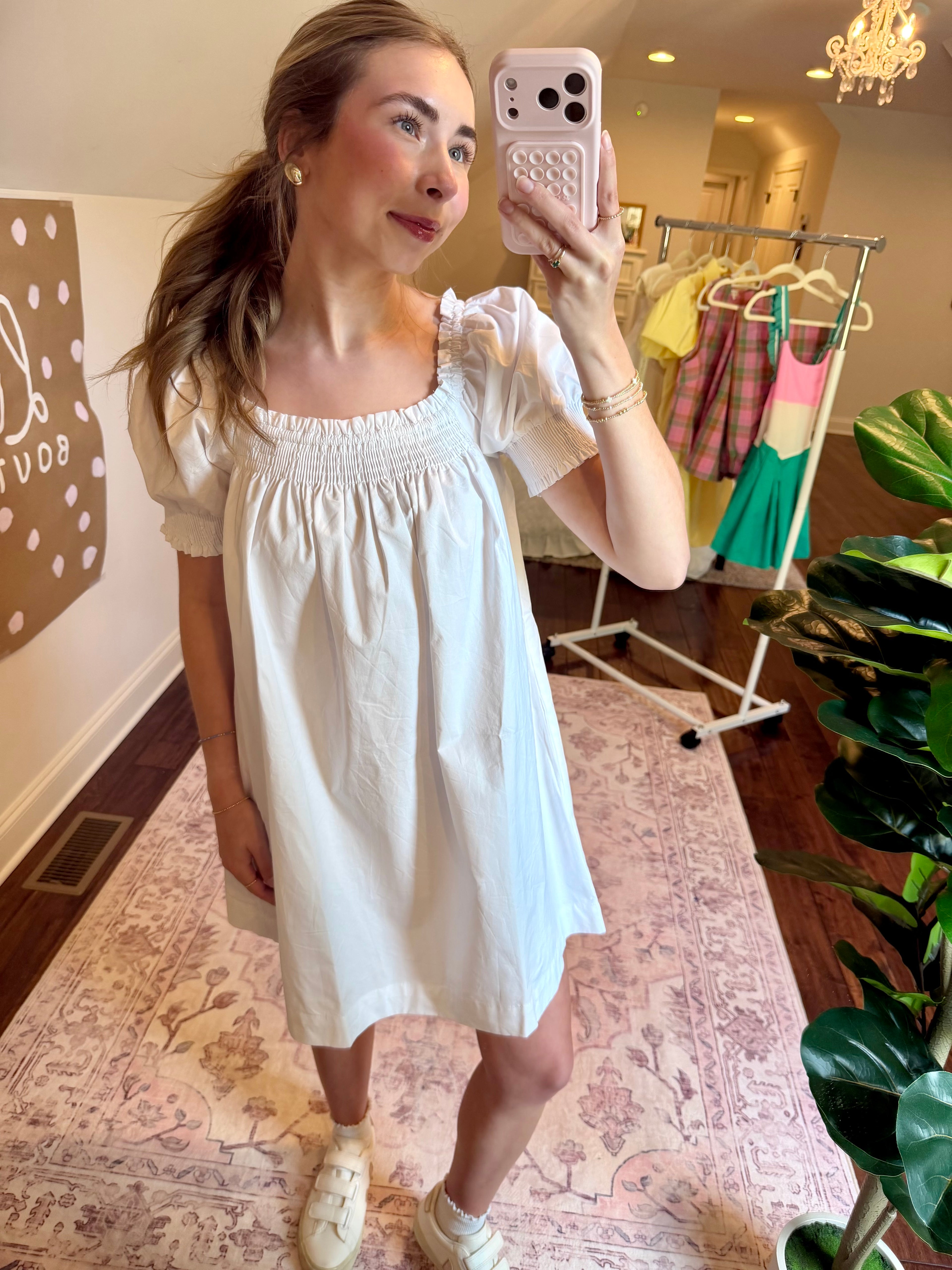Woman taking a mirror selfie wearing a white dress in a store.