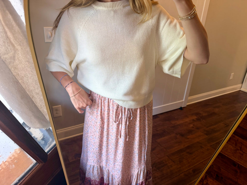 Person wearing a white sweater and pink skirt standing in front of a mirror.