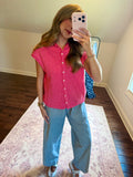 A woman takes a mirror selfie in a room, wearing a bright pink short-sleeve button-up shirt and light blue wide-leg jeans.