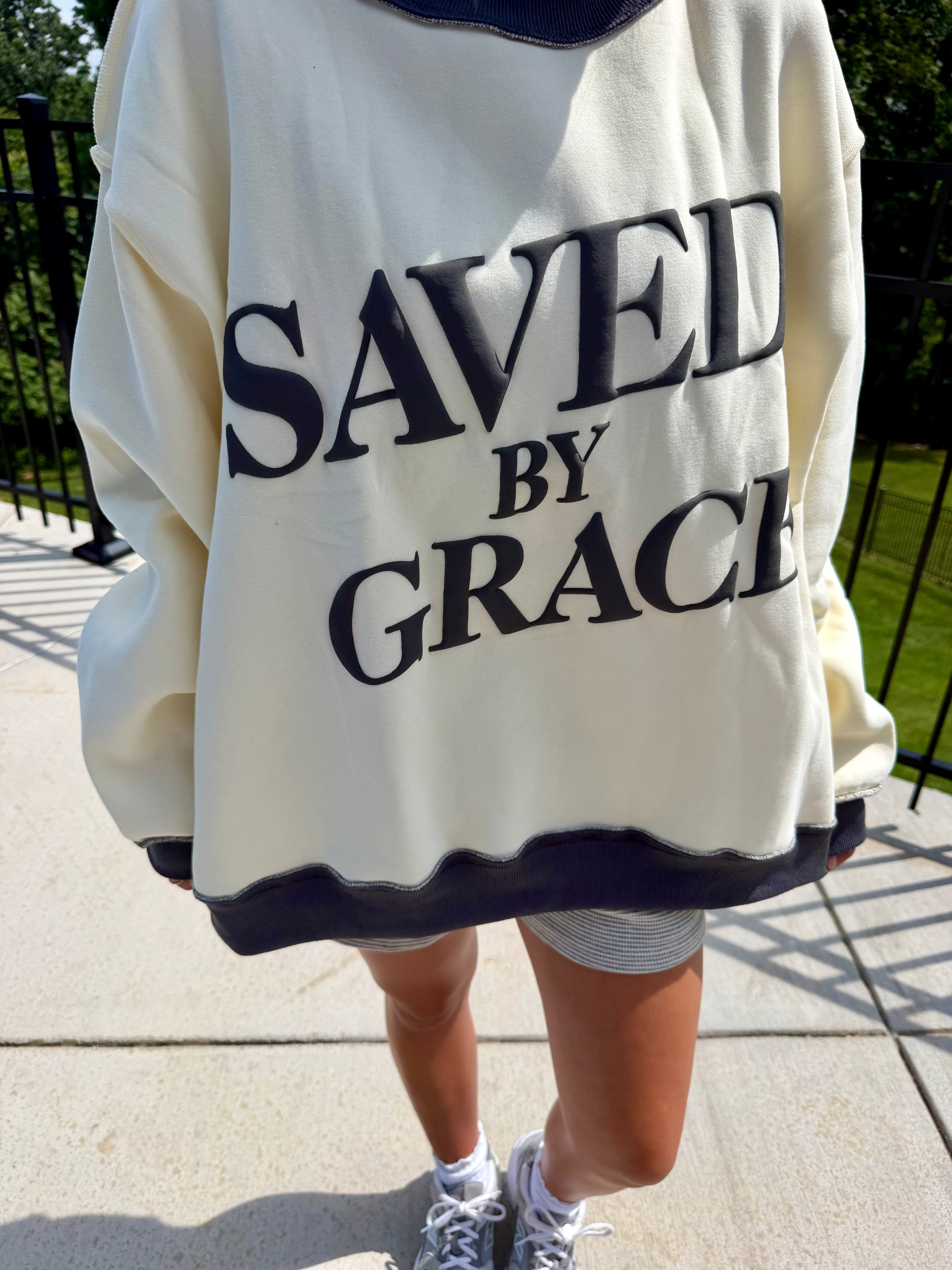 Person wearing a white sweatshirt with 'SAVED BY GRACE' text on a sidewalk.