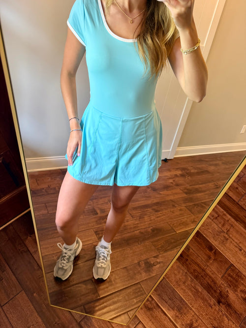 Person wearing a light blue dress standing in front of a mirror on a wooden floor.