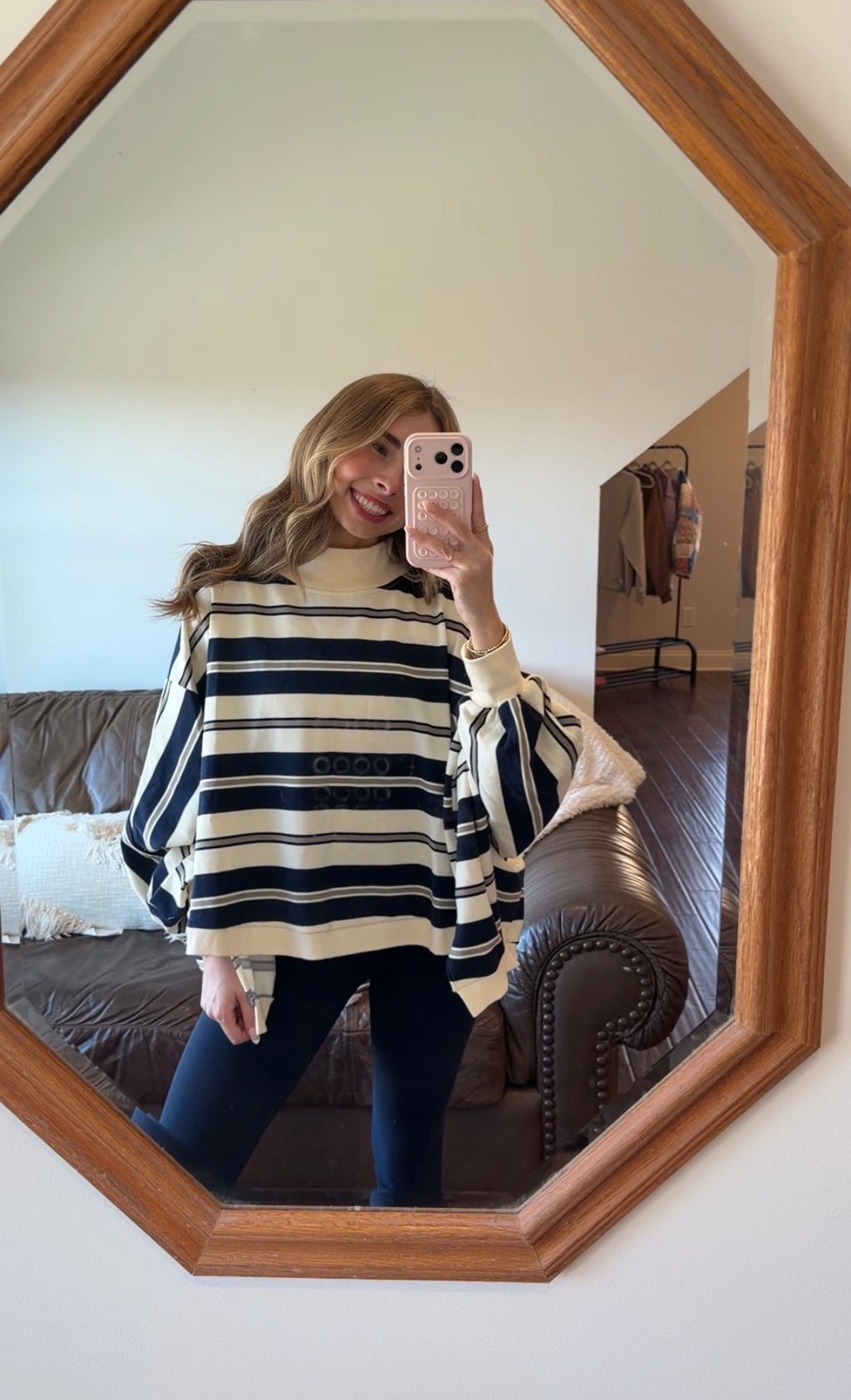Person wearing a striped sweater taking a mirror selfie in a room with a bed and wooden furniture.