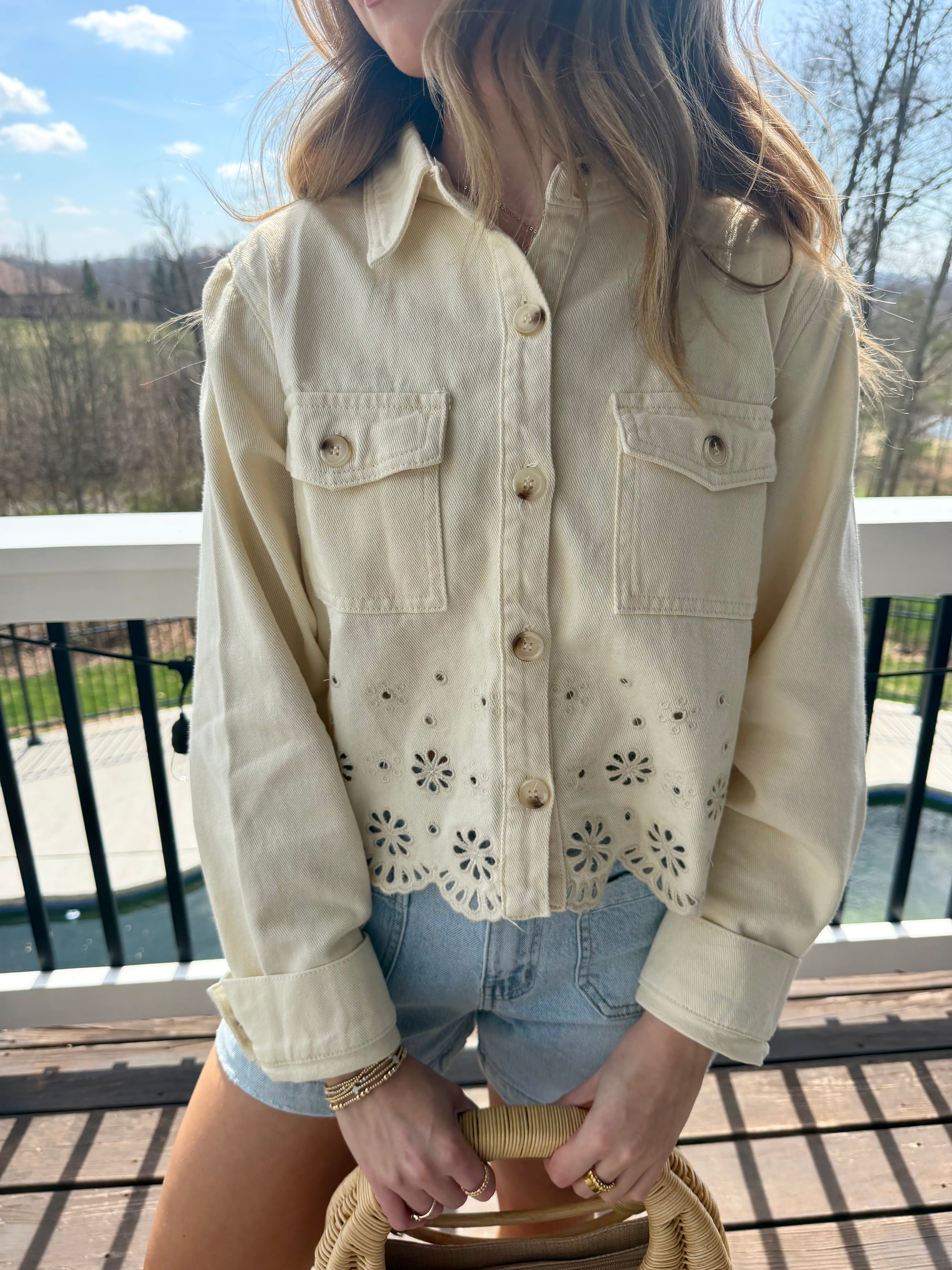 Person wearing a light-colored denim jacket with floral cut-out details outdoors.