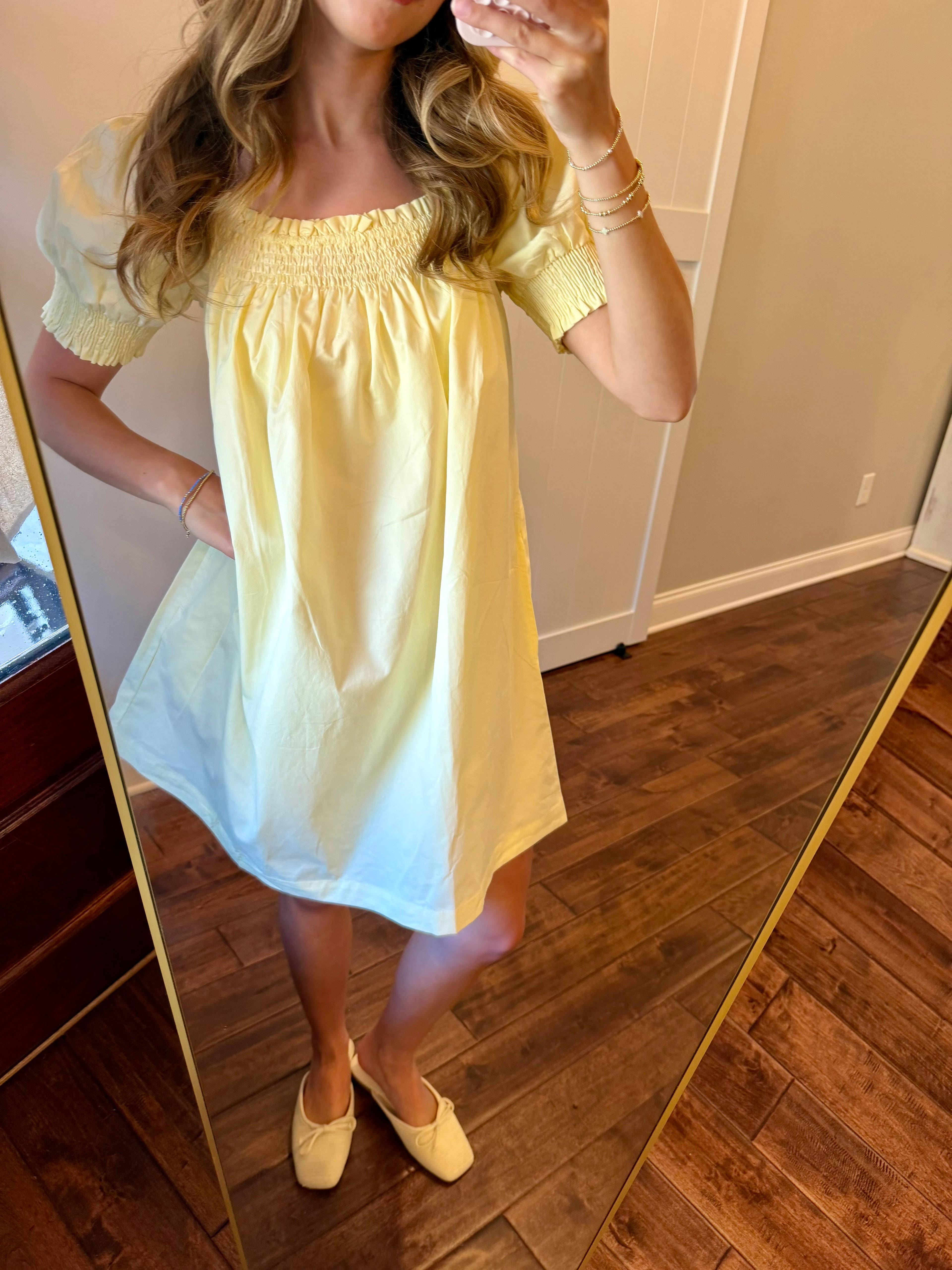 Woman wearing a yellow dress standing in front of a mirror.