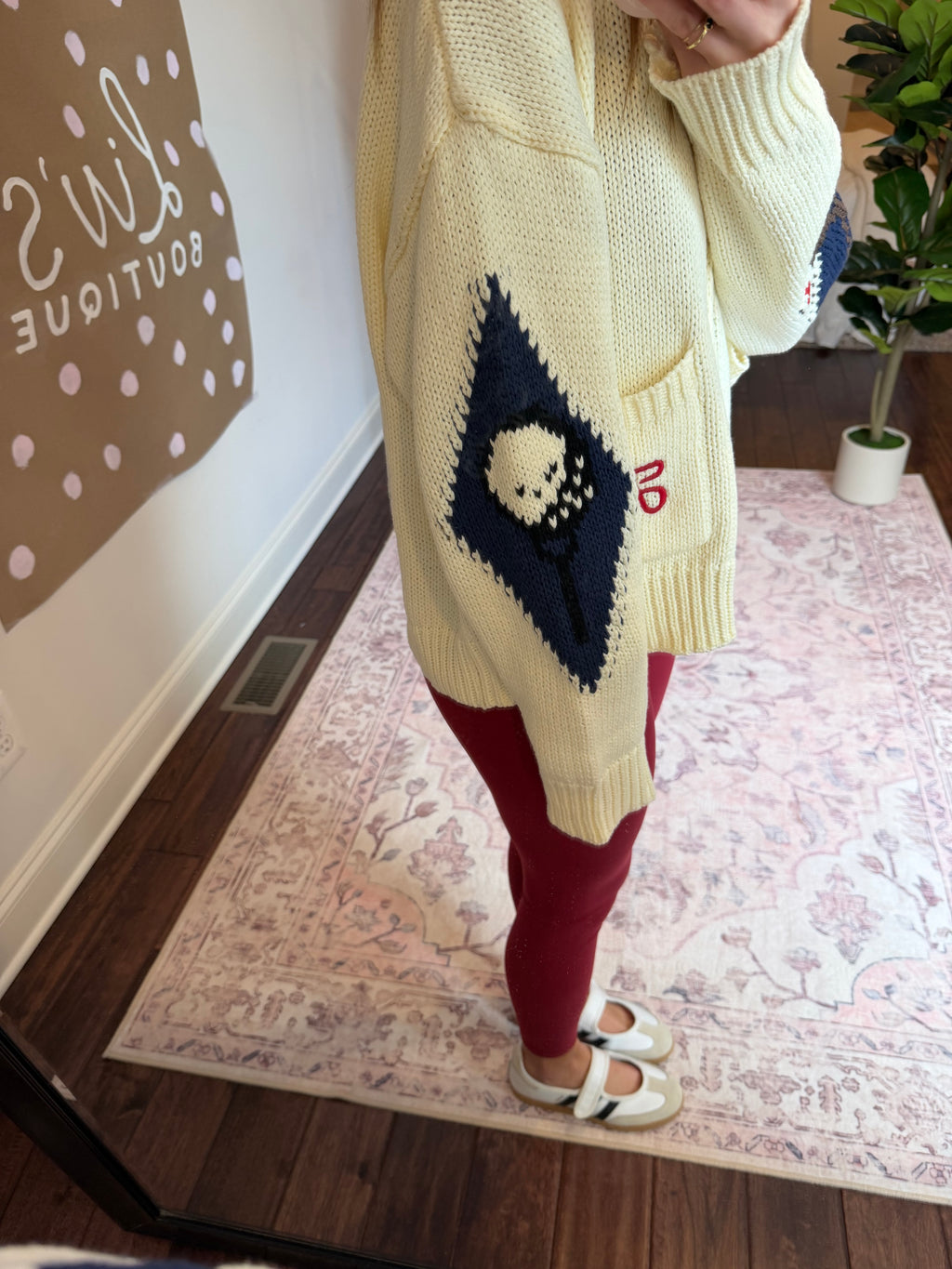 Person wearing a white sweater with green and red patterns, standing on a patterned rug.