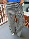 Black and white gingham wide-leg pants worn by a person standing on a porch with a brick wall and white railing in the background.