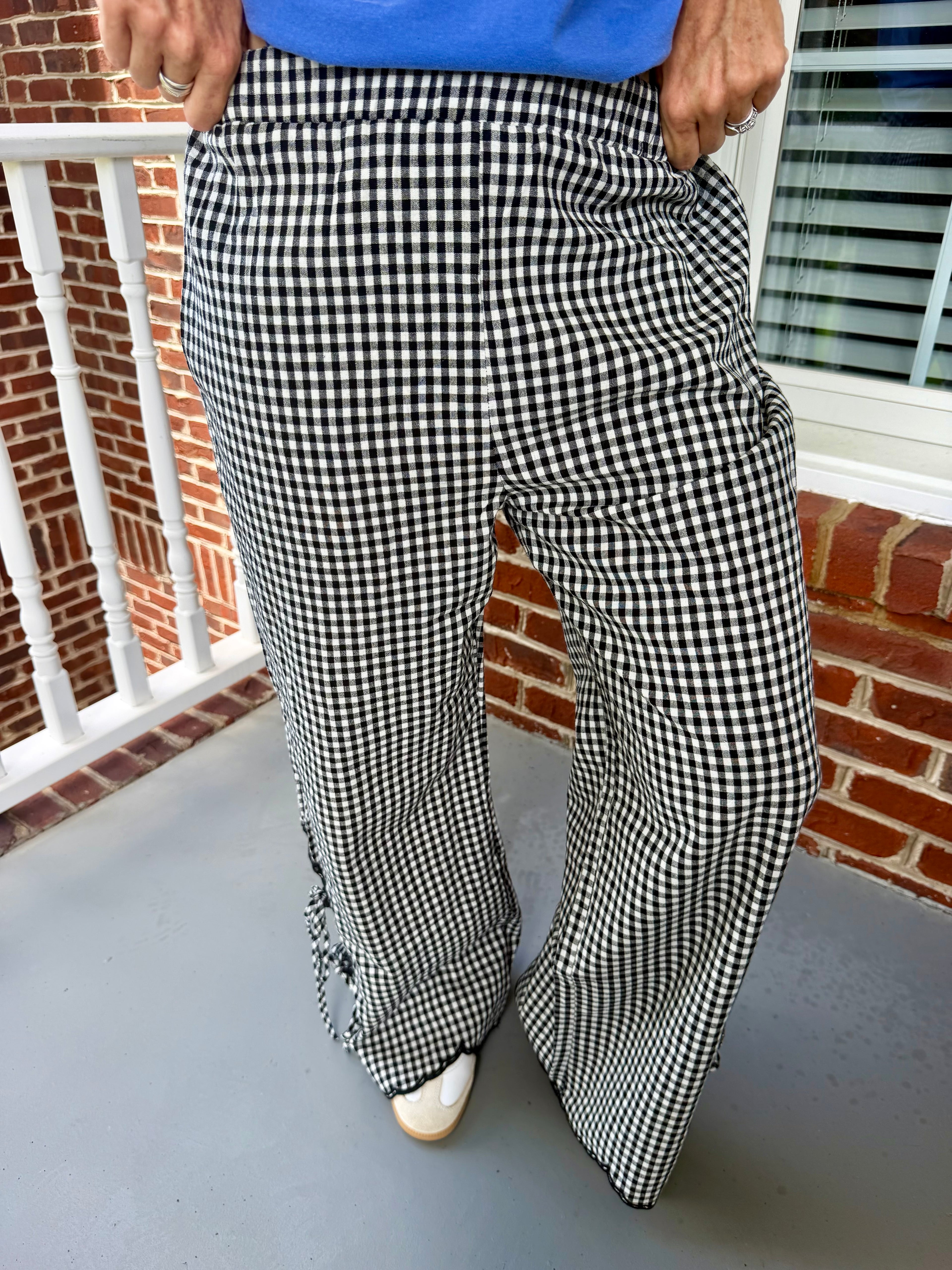 Black and white gingham wide-leg pants worn by a person standing on a porch with a brick wall and white railing in the background.