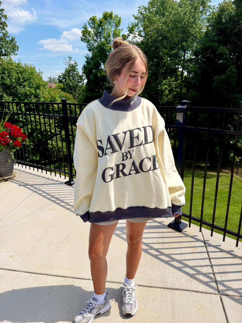 Person wearing a 'SAVED BY GRACE' sweatshirt outdoors on a sunny day.