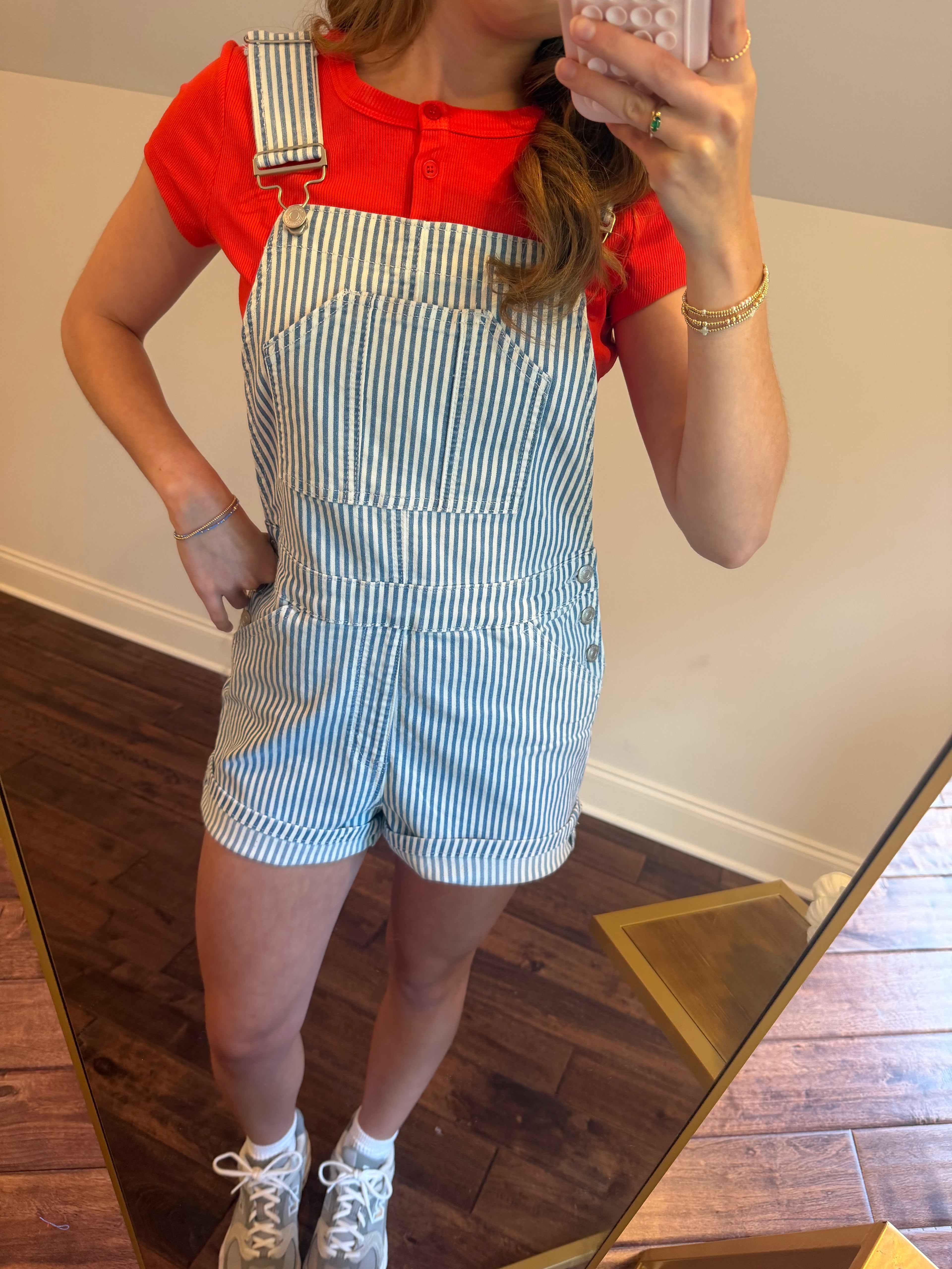 Person wearing a red shirt and blue striped overalls taking a mirror selfie.