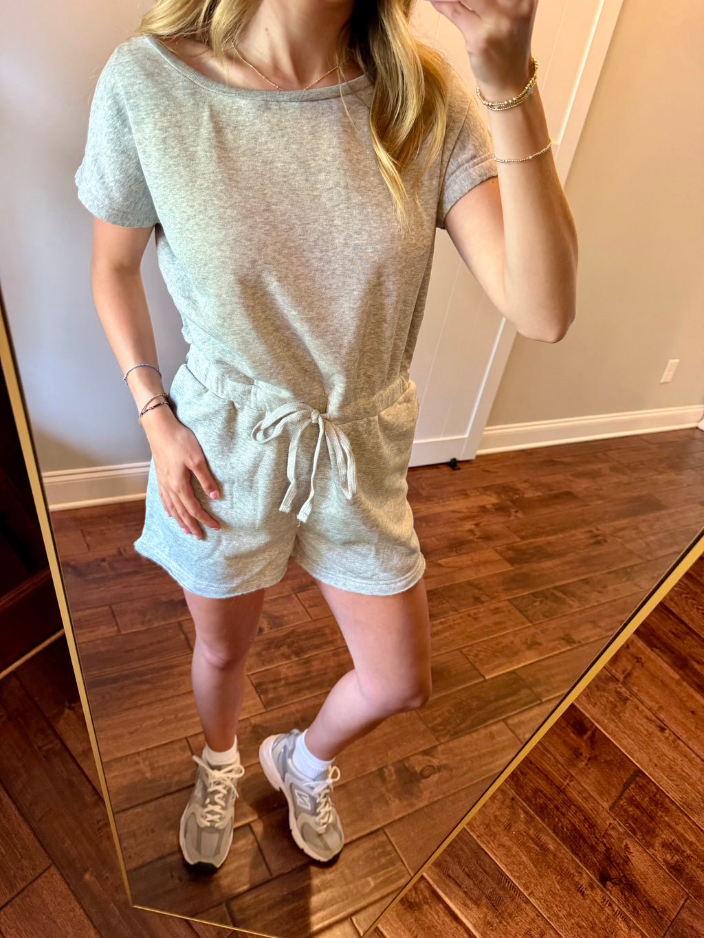 Person wearing a light gray romper in a room with wooden flooring.