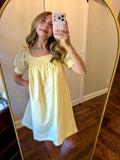 Woman taking a mirror selfie wearing a yellow dress in a room with wooden flooring.