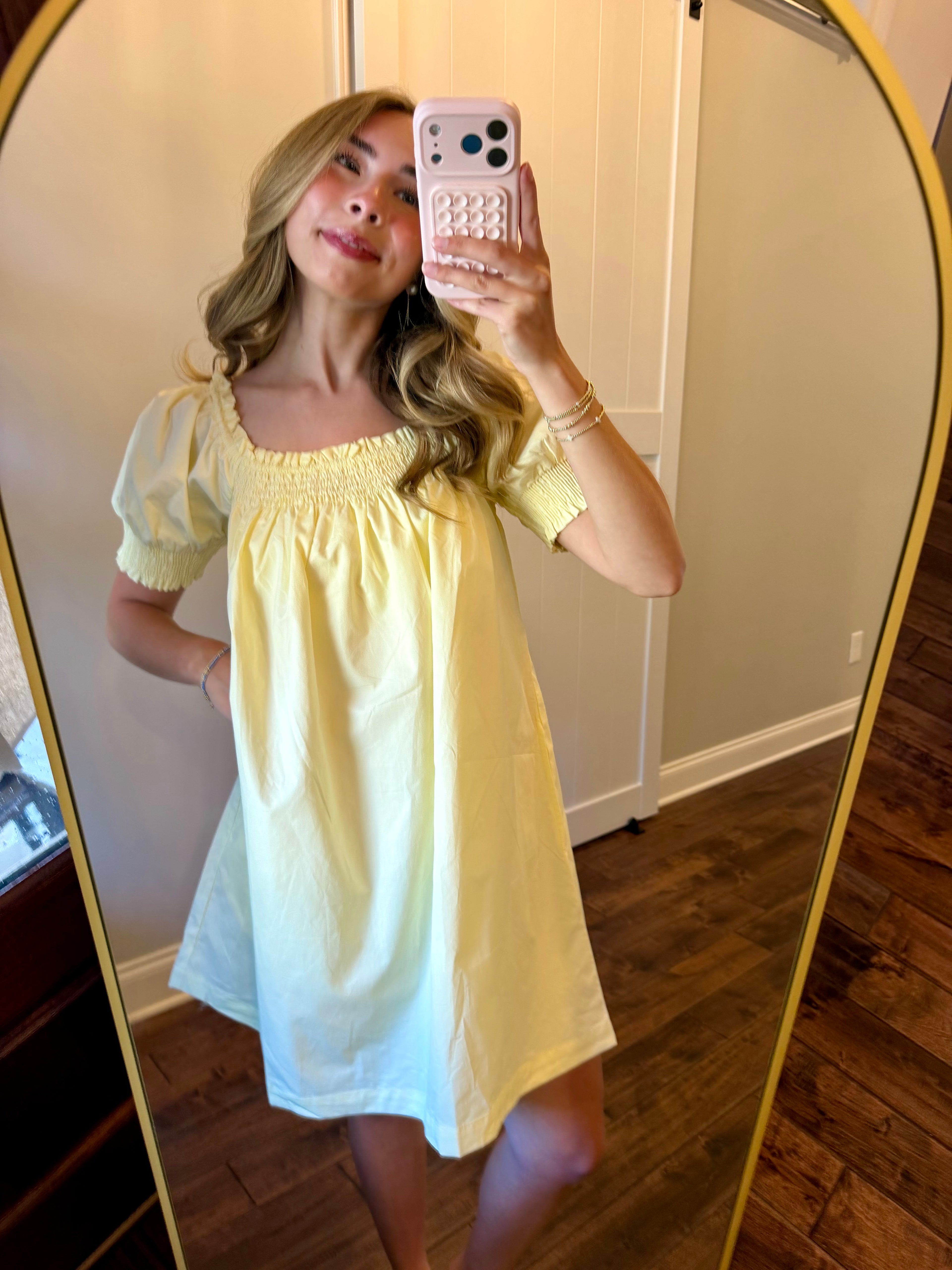 Woman taking a mirror selfie wearing a yellow dress in a room with wooden flooring.