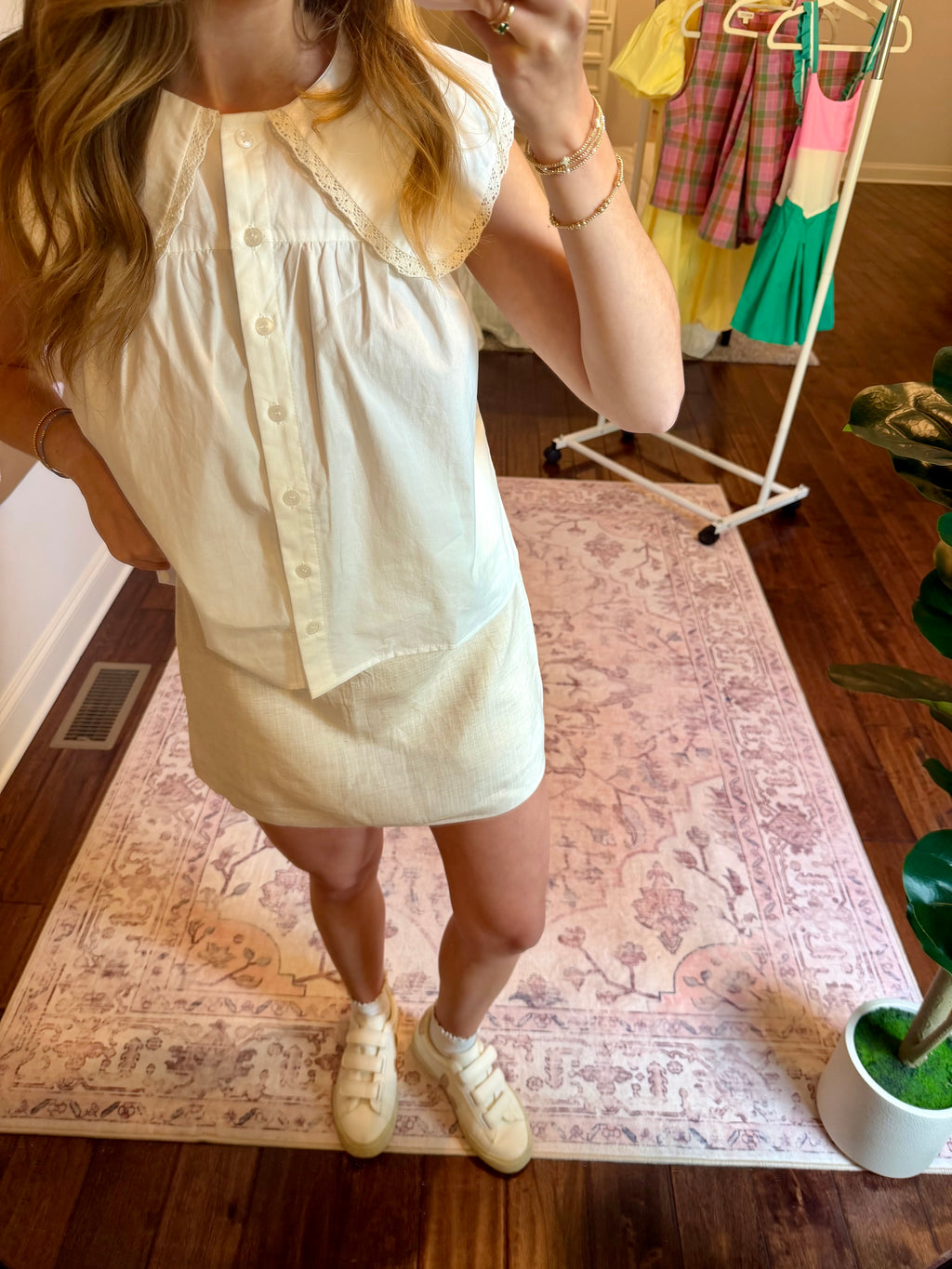 Person wearing a cream skirt and white top with a patterned rug and wooden floor in the background