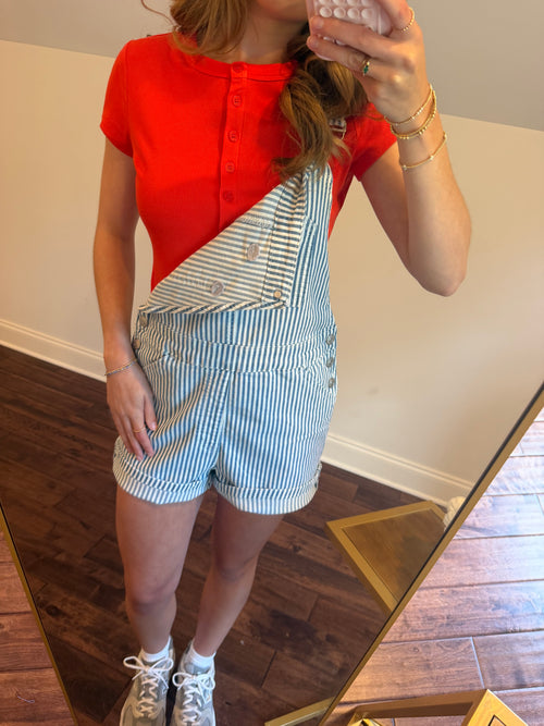 Person wearing a red top and blue and white striped shorts in a room with wooden floor.