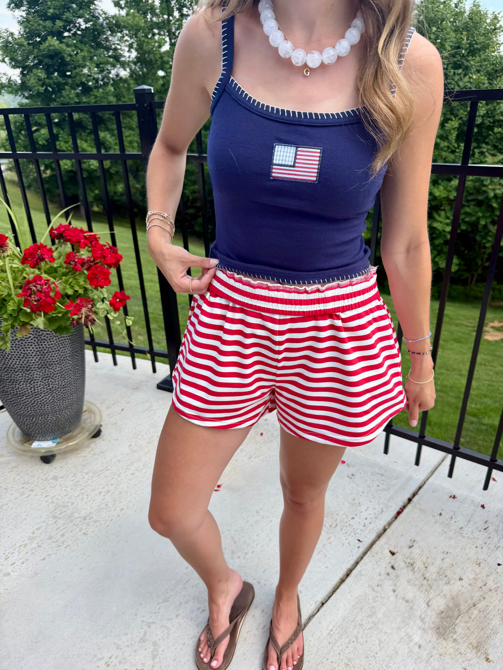 Woman wearing a blue top with an American flag design and red and white striped shorts on a patio.