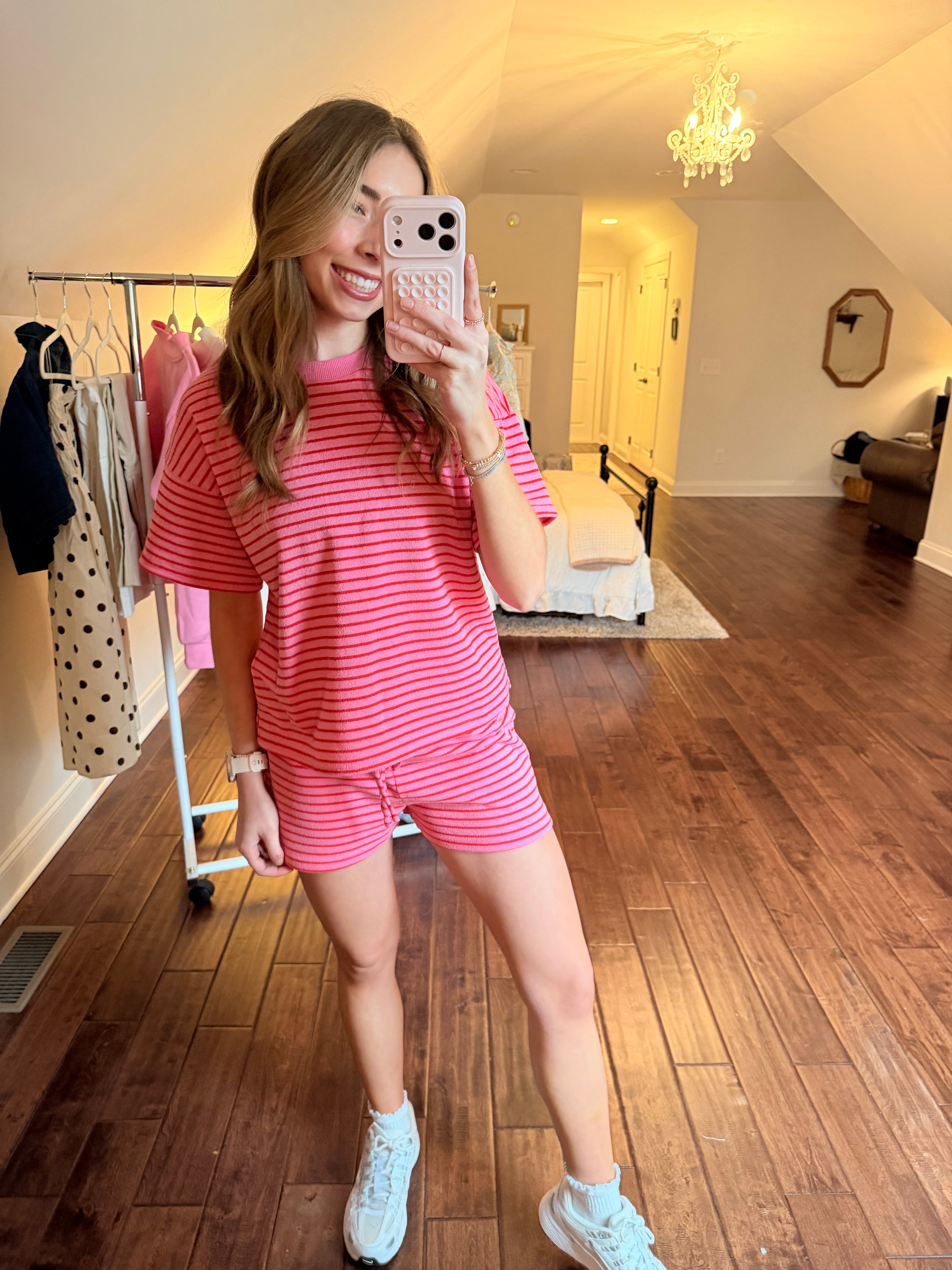 Person taking a mirror selfie wearing a pink matching set in a room with wooden floor and white walls.