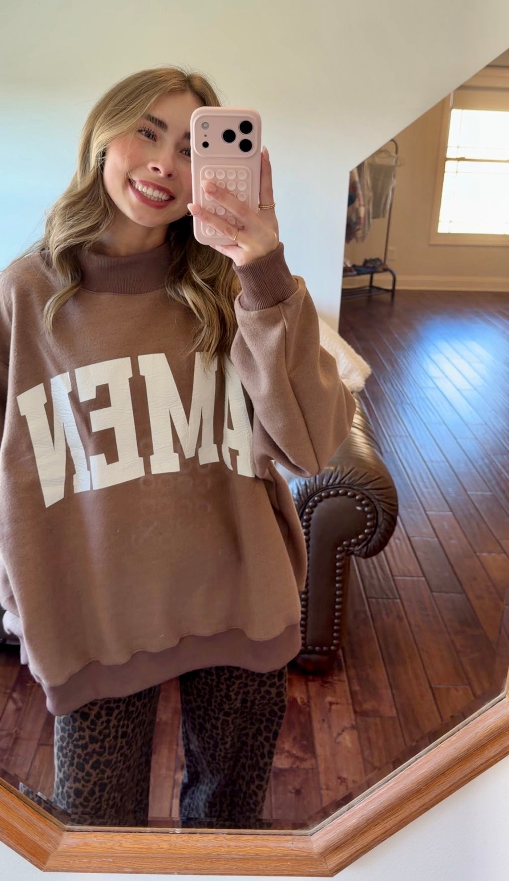Person wearing a brown sweatshirt with 'AMEN' printed on it, taking a mirror selfie.